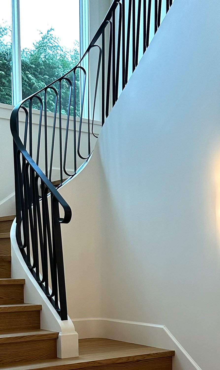 Modern interior staircase with custom black steel railing beside large window