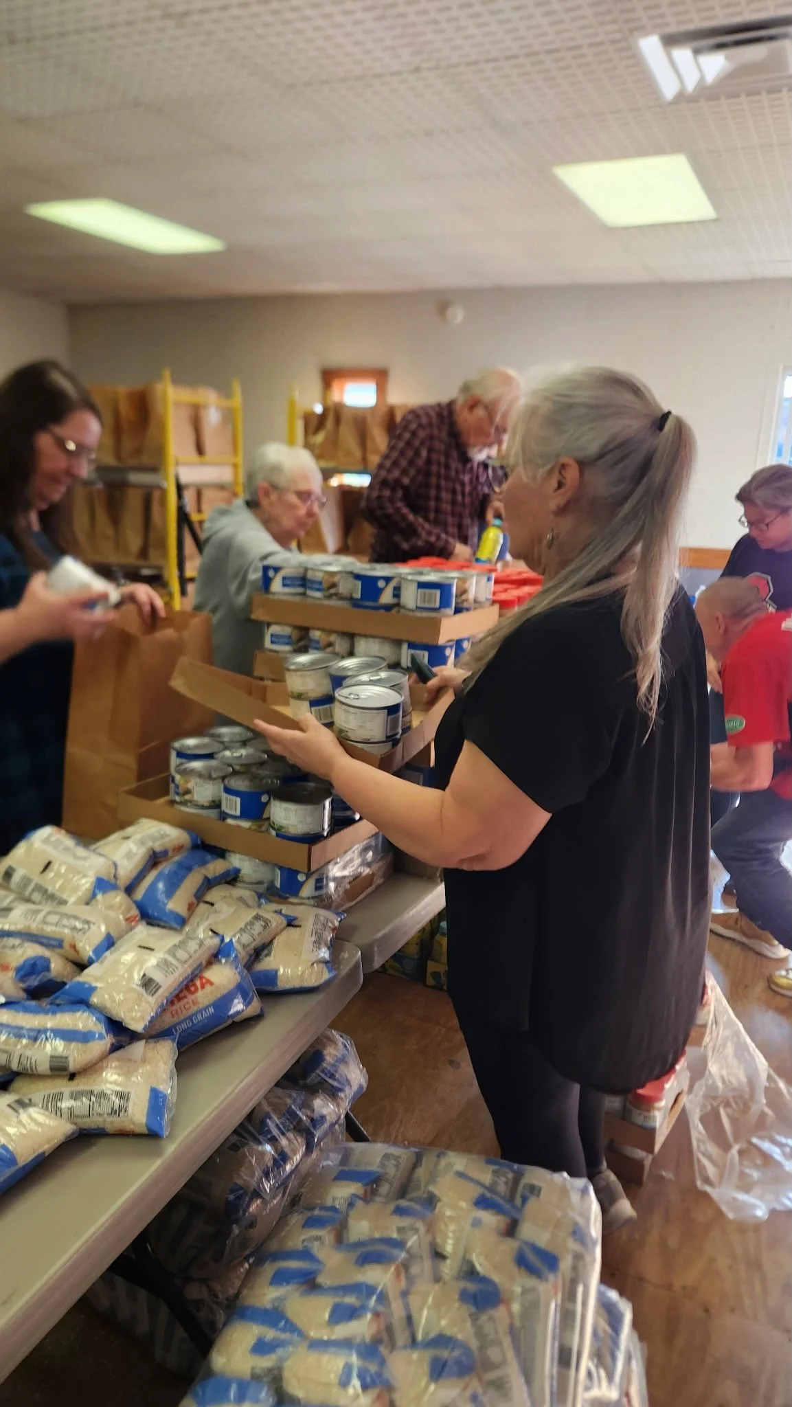 People volunteering at a food bank sorting and packing canned goods and packages of rice and beans.