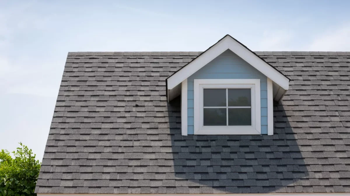 Close-up of a white house with tiled gabled roof, windows with shutters, and a clear blue sky.