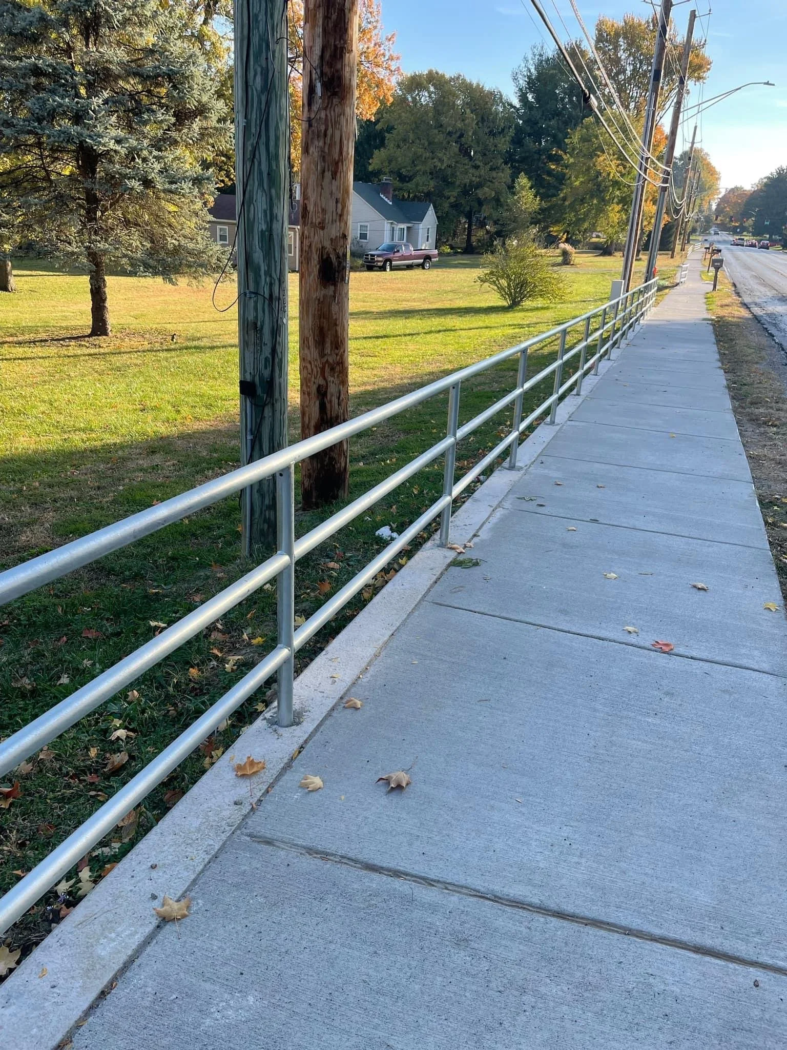 Empty sidewalk running alongside a grassy area with trees and utility poles, in a suburban neighborhood during daytime.