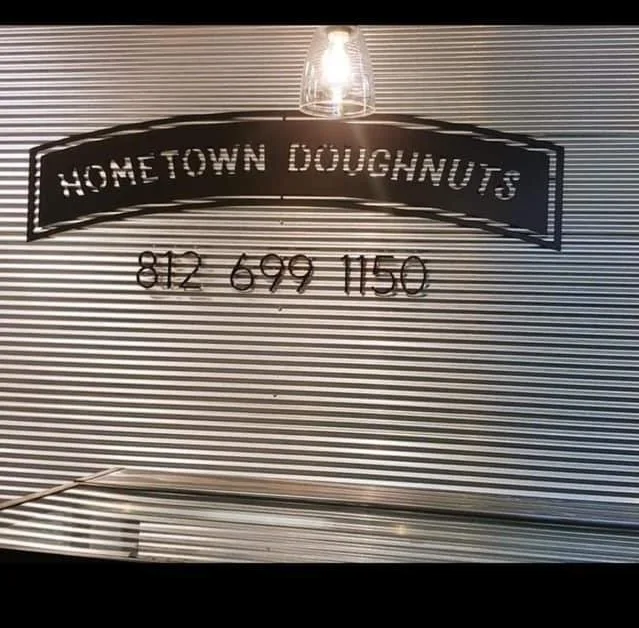 Sign for Hometown Doughnuts with phone number 812-699-1150 on a corrugated metal surface