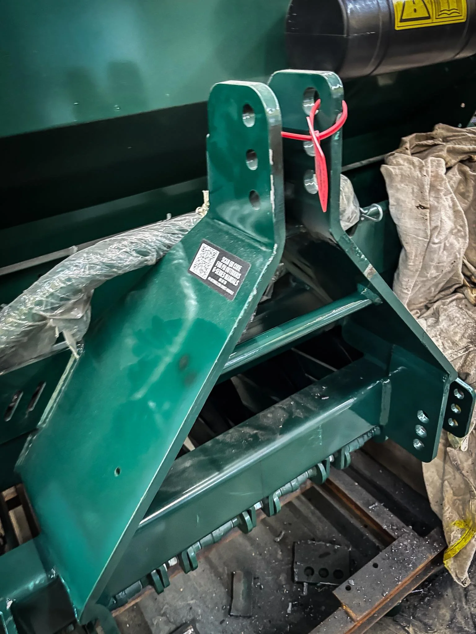 Close-up of a green metal industrial machine part with bolts and wiring, surrounded by protective and packaging materials.