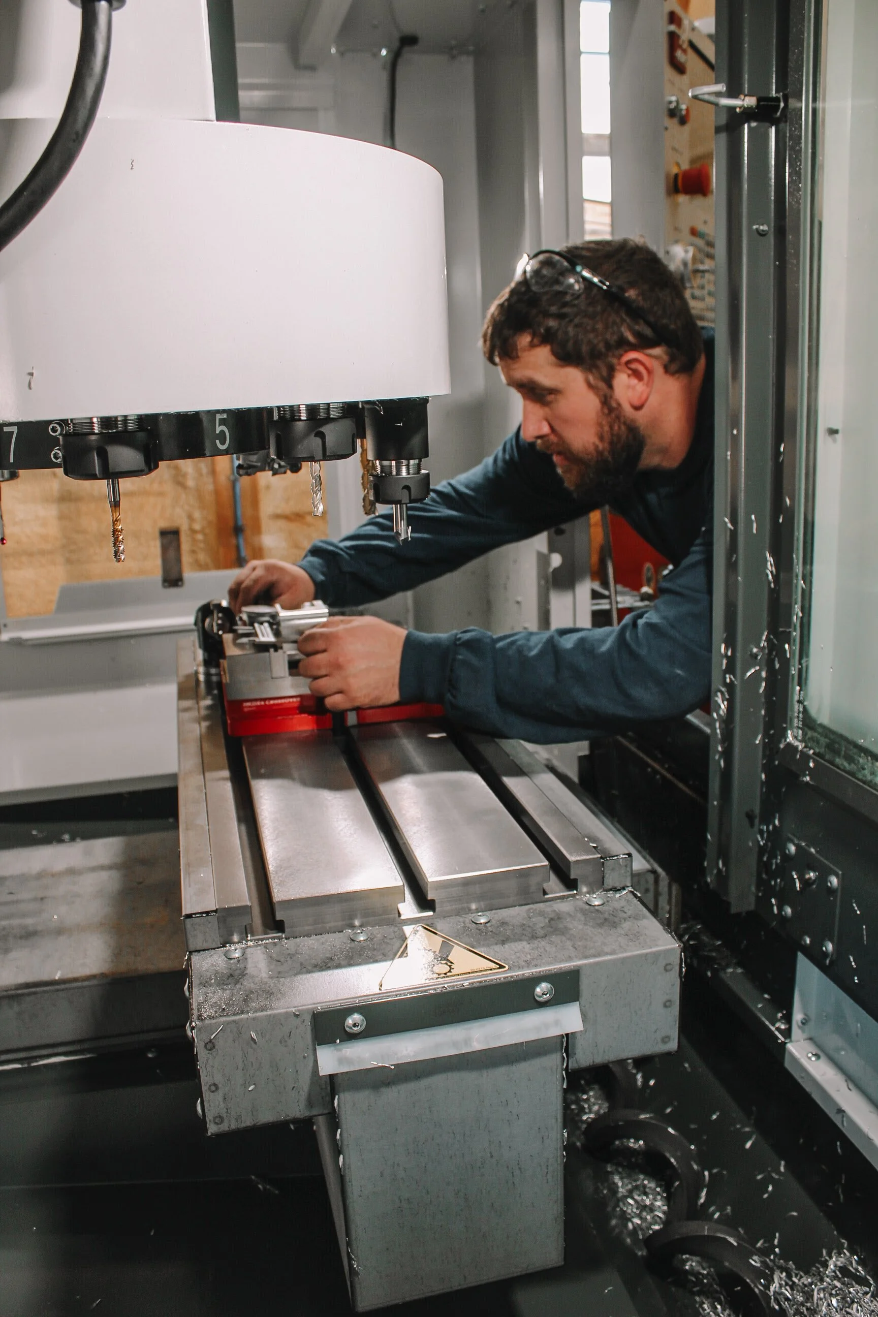 A man wearing safety glasses working with a CNC machine in a workshop or factory setting.
