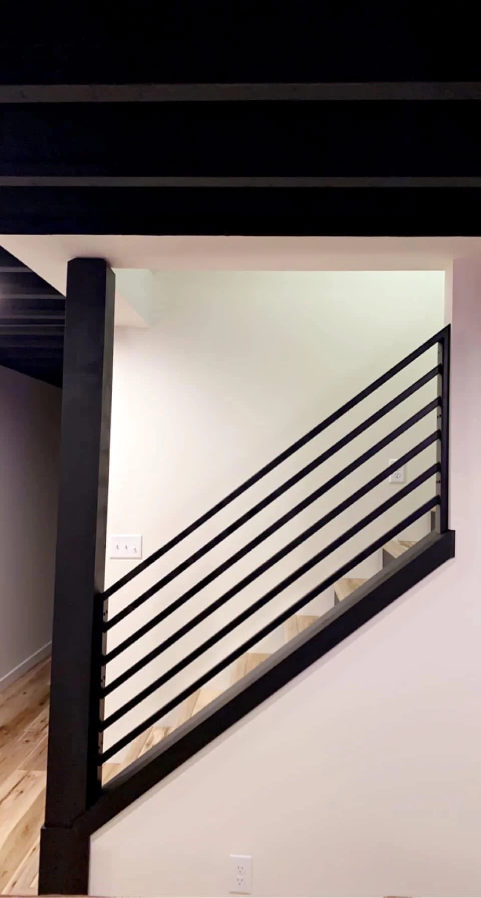 Interior view of a modern staircase with a black metal railing and wooden stairs in a residential home.