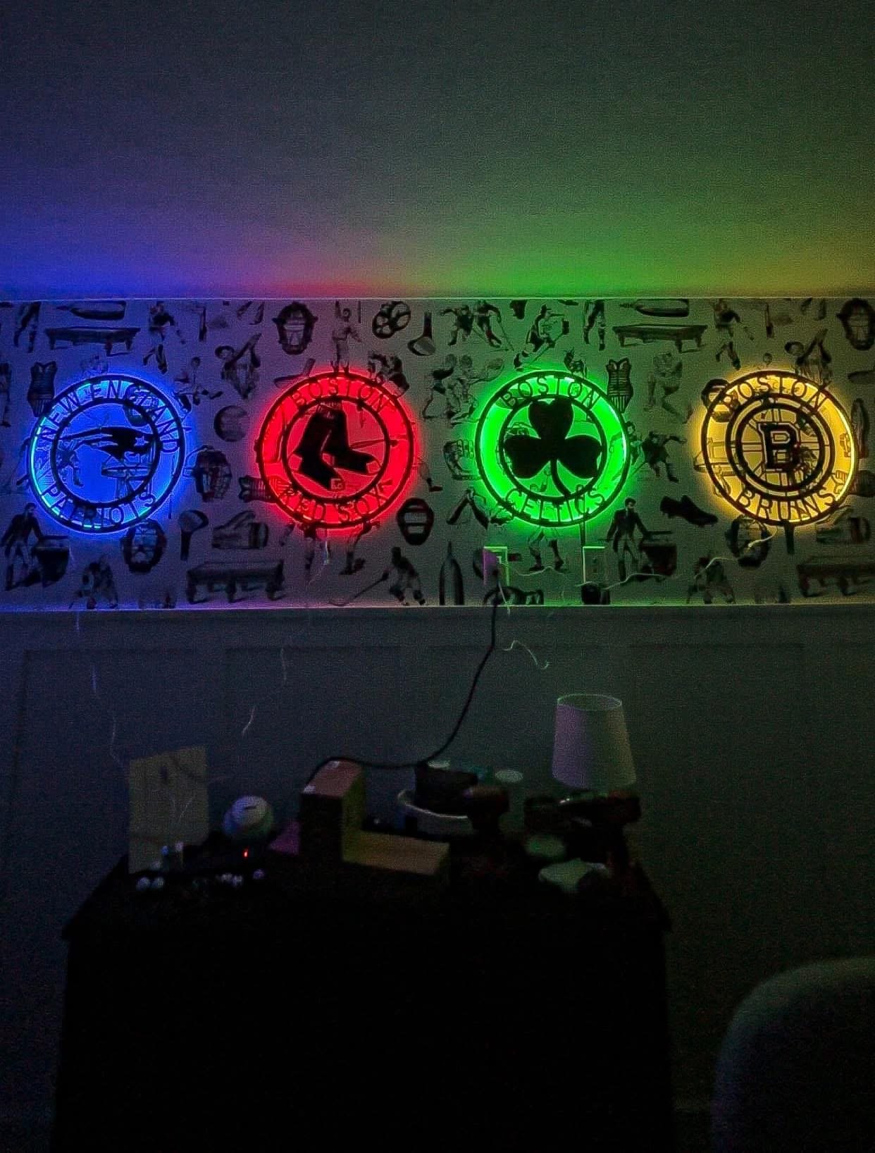 Wall decorated with illuminated Boston sports team logos in blue, red, green, and yellow, with gym or fitness-themed illustrations in the background.