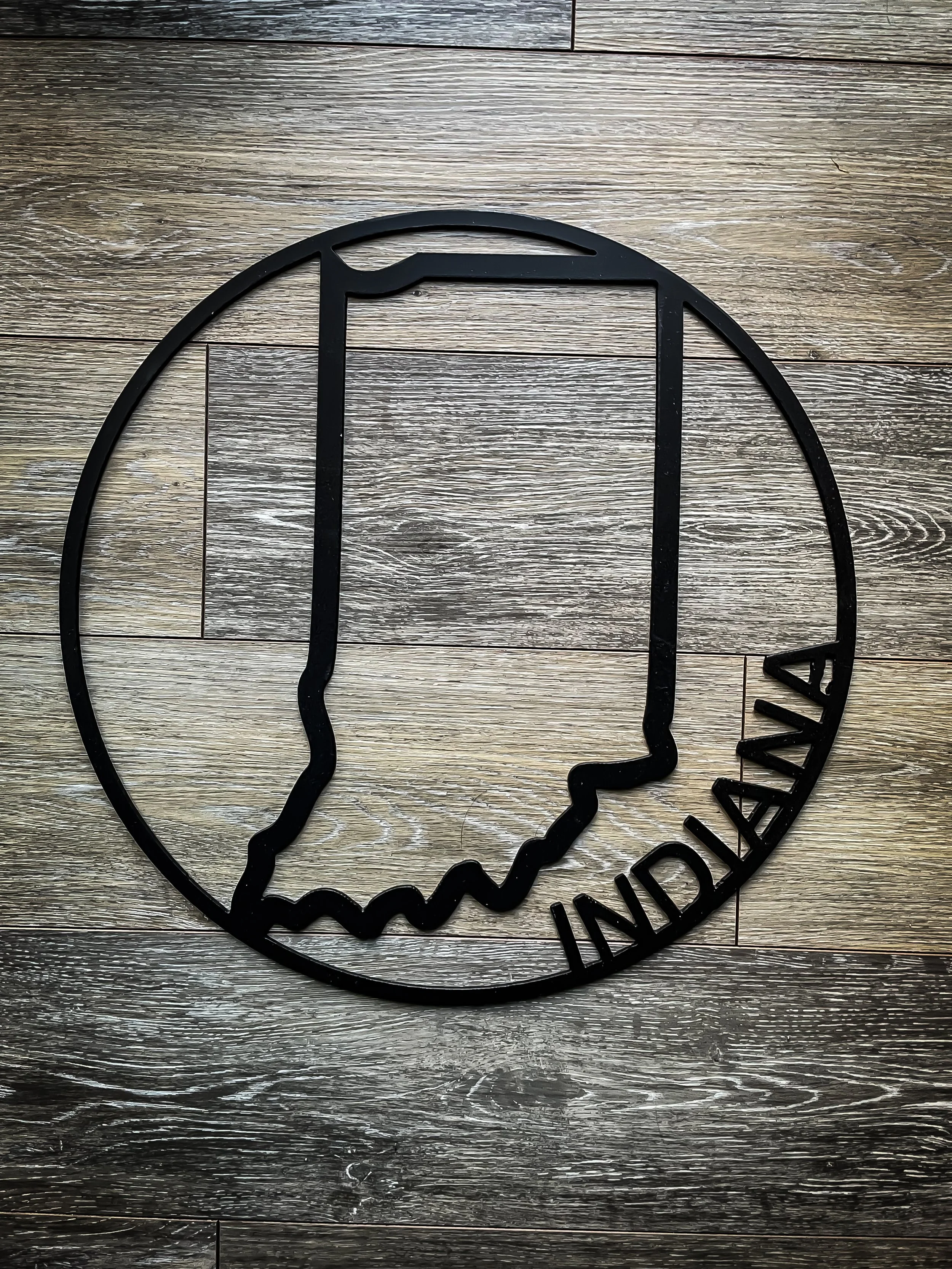 Black metal sign featuring a silhouette of a man's profile with the word 'WANDALAY' written underneath, placed on a wooden floor.