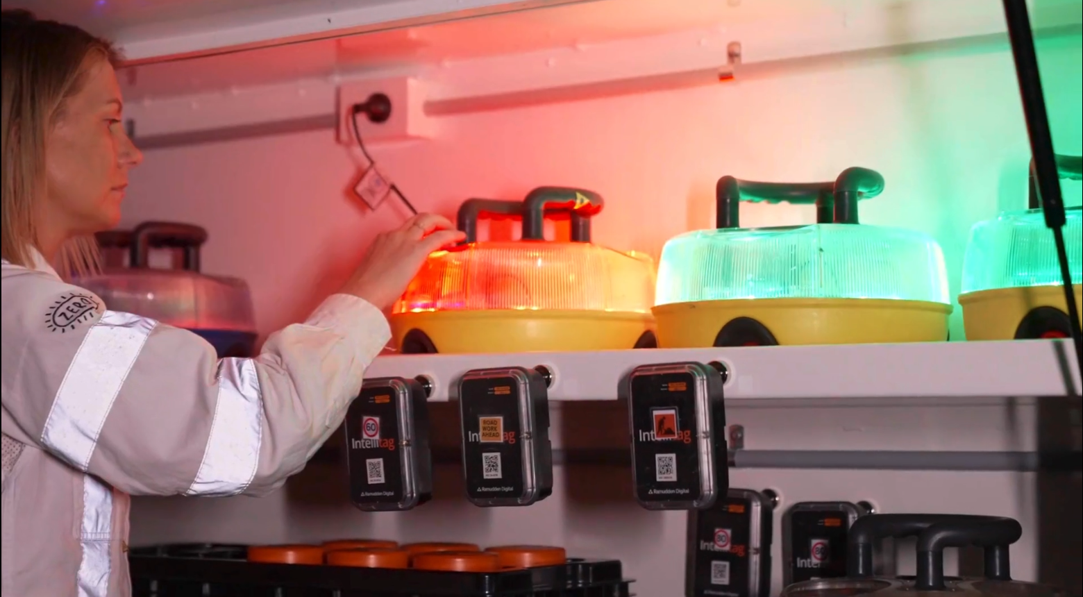 A woman adjusting a large, yellow, illuminated, container-like device on a shelf, with similar lit containers and electronic devices below on the shelf.