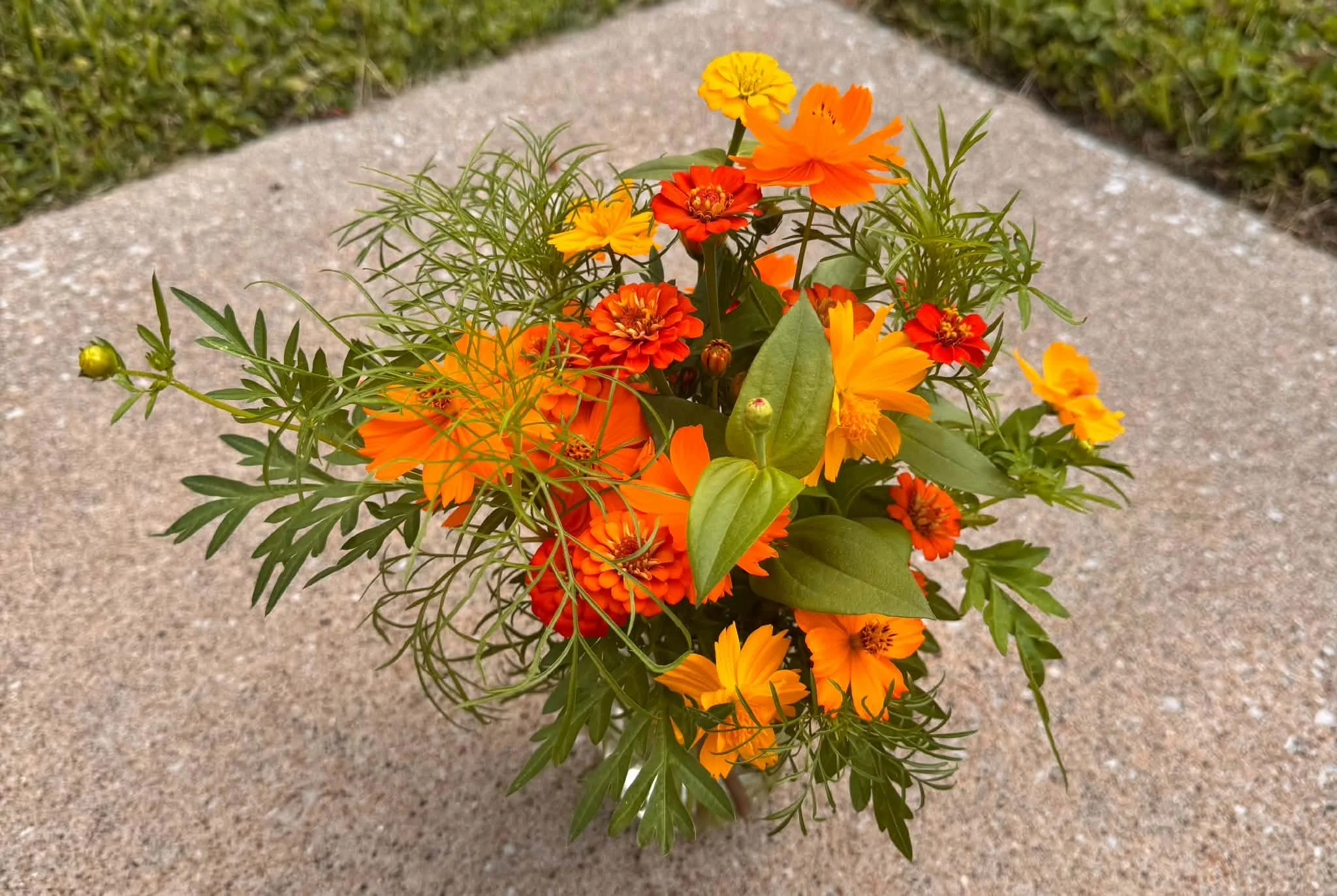 A bouquet of orange and yellow flowers with green leaves on a concrete surface.