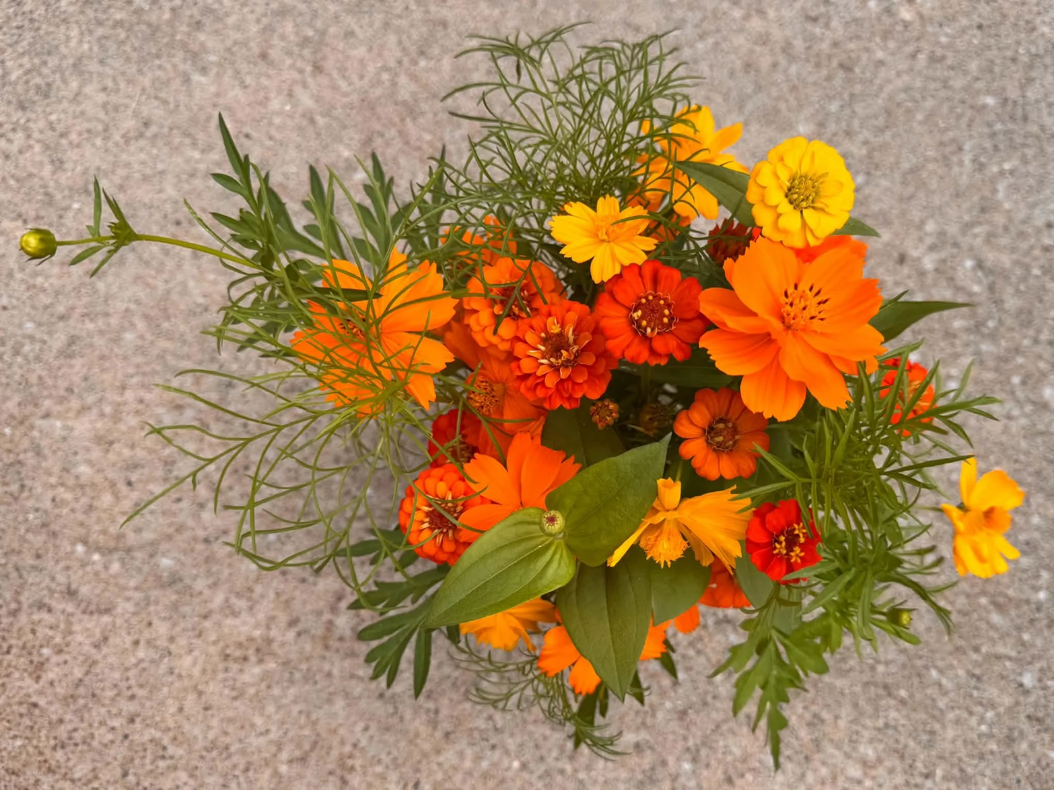 A bouquet of orange and yellow flowers with green foliage on a gray speckled surface.