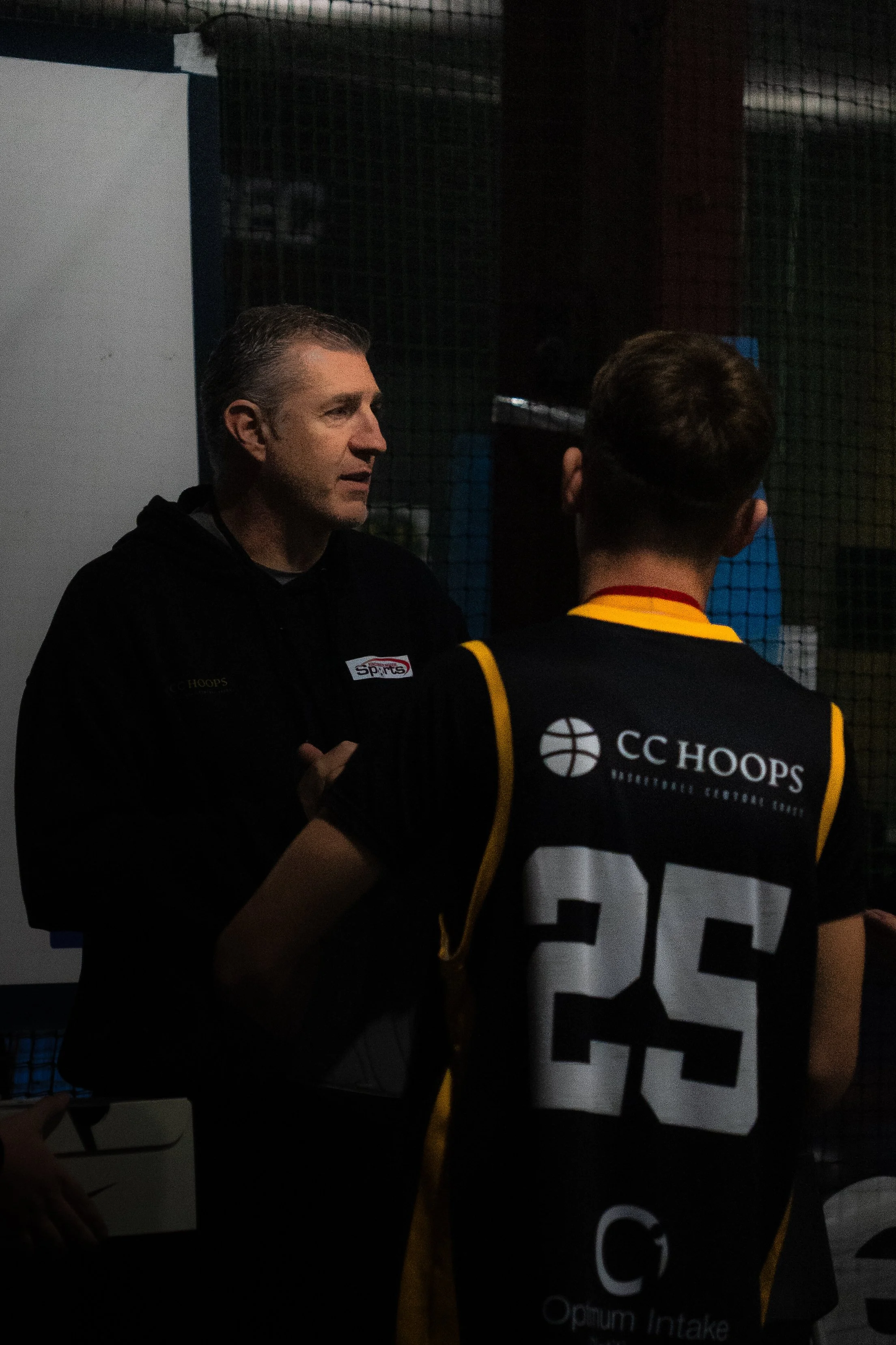 A coach and a basketball player having a discussion during a game or practice, with the player wearing a black jersey numbered 25.