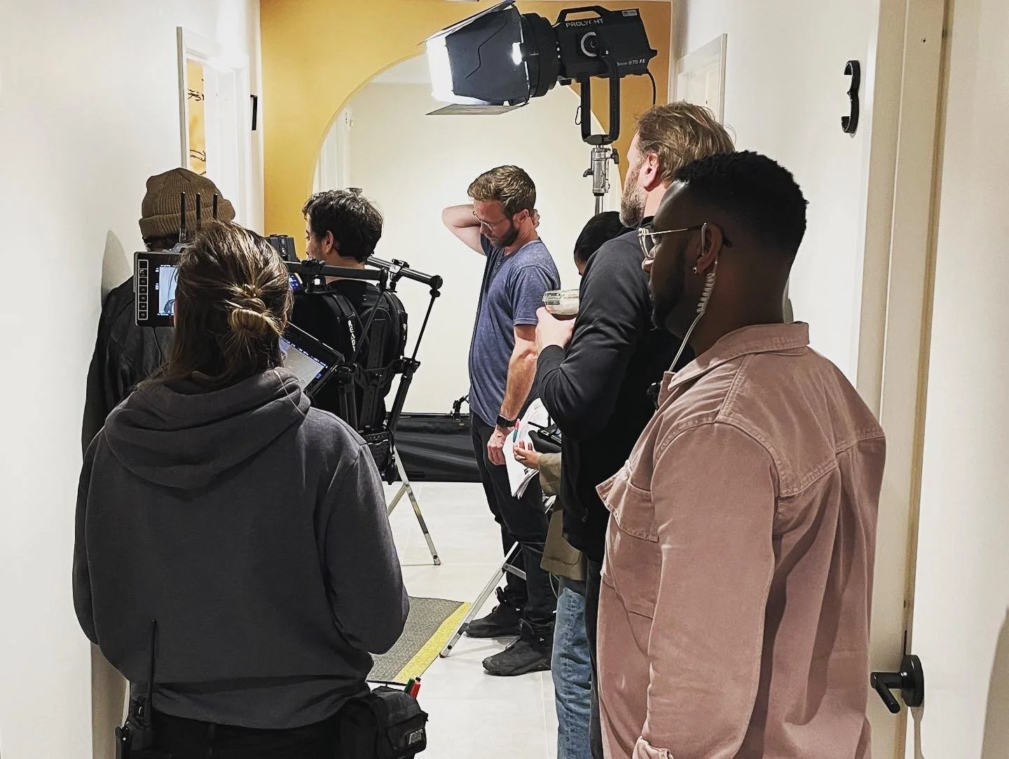 Film crew on set in a hallway with a camera, lighting equipment, and several crew members preparing for a shot.