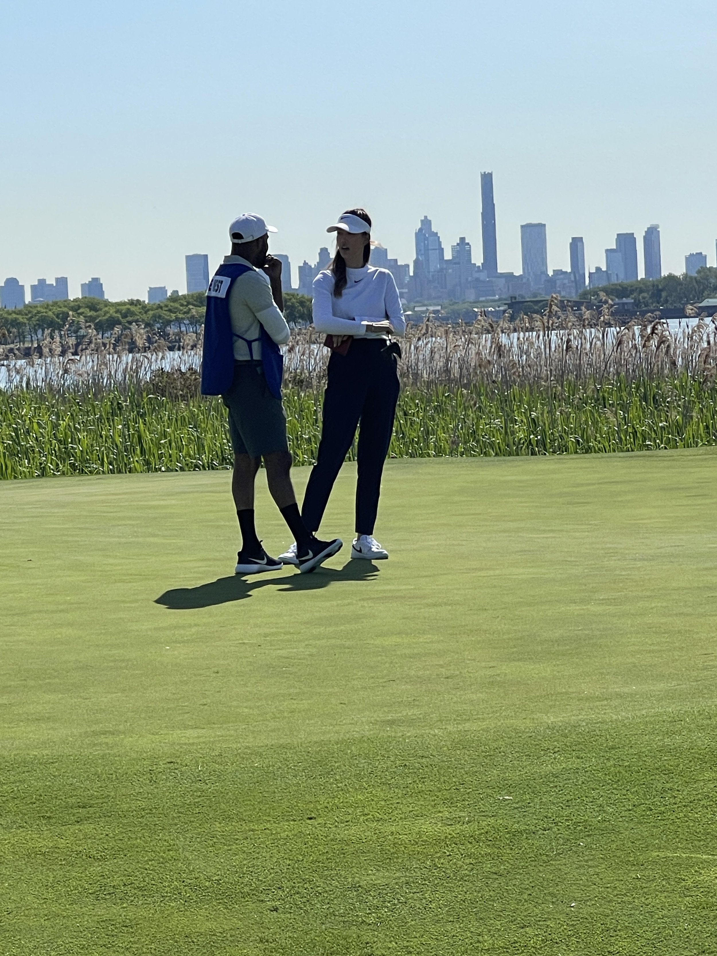 A man and a woman having a conversation on a golf course with a city skyline in the background.