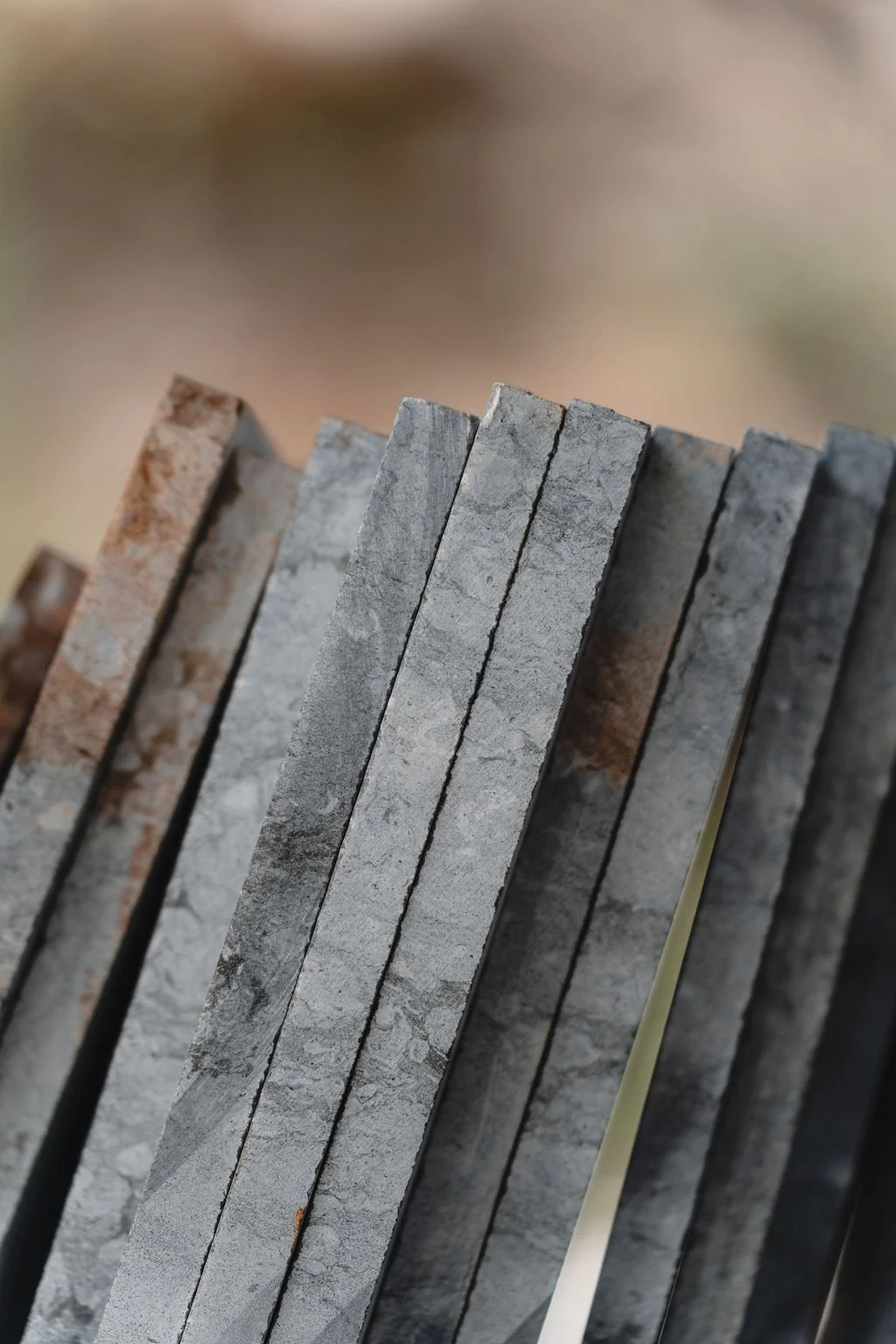 Close-up of a row of grey concrete or stone slabs with slightly rough texture, leaning against each other at an angle, with a blurred background.