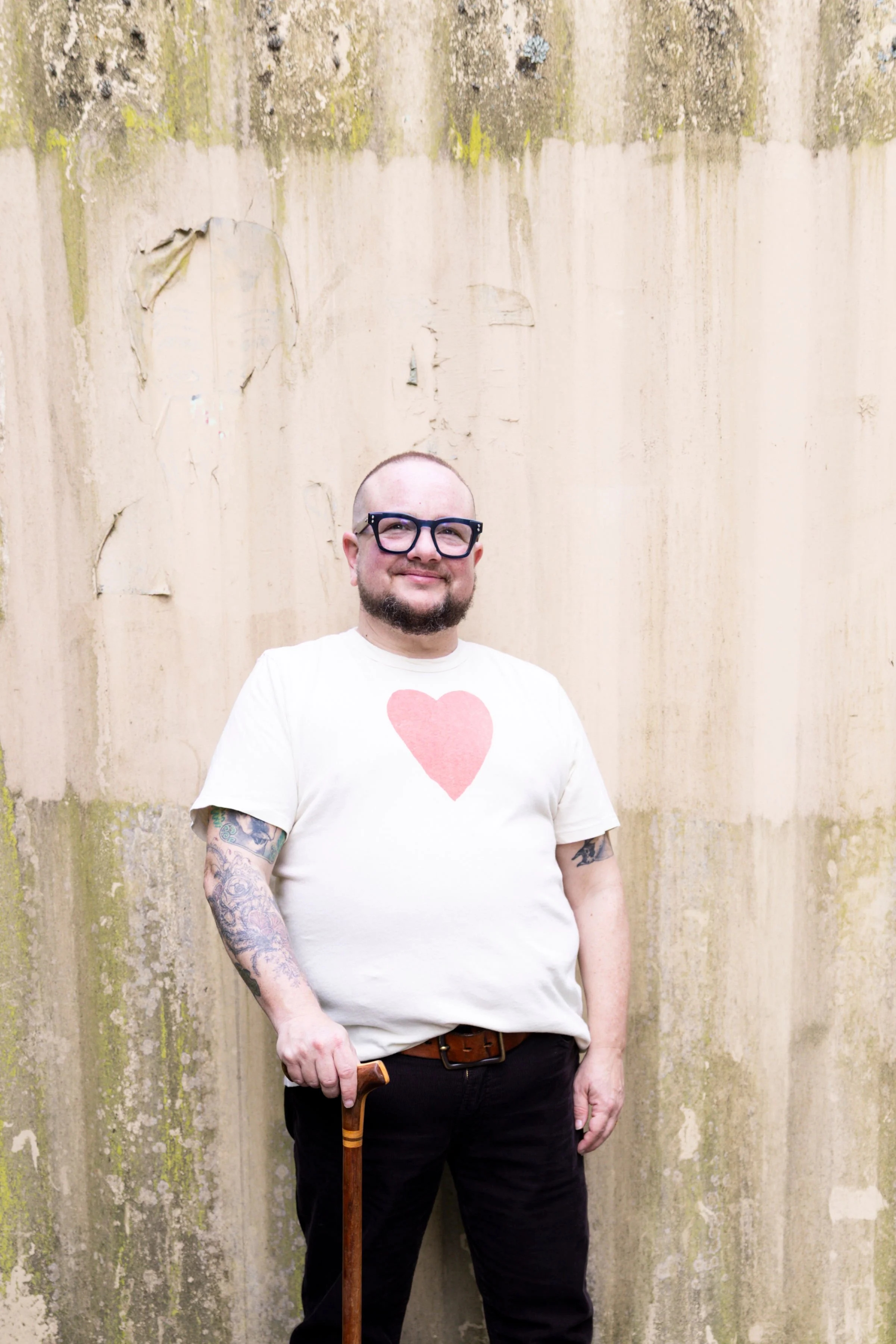 Photo: Elliot Kukla is wearing a yellow shirt and is standing with a cane under a shaded tree.