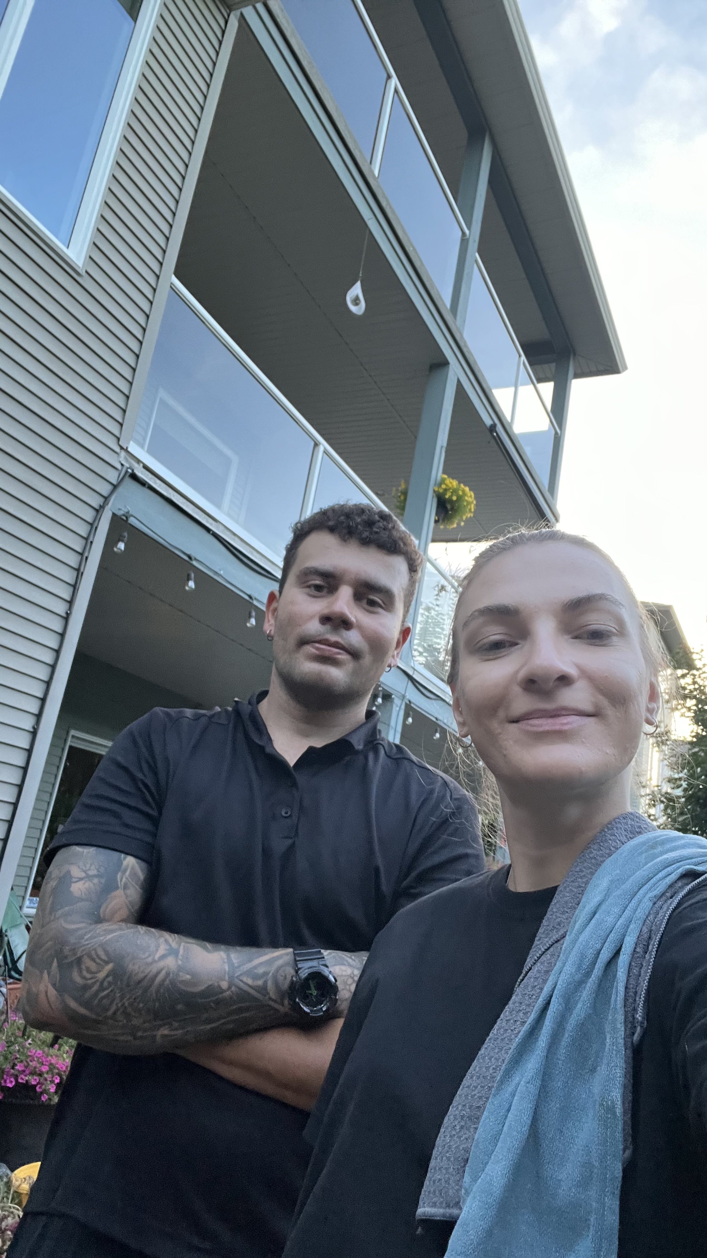 Two people taking a selfie outside a multi-story residential building with glass balconies after cleaning all windows on each level.