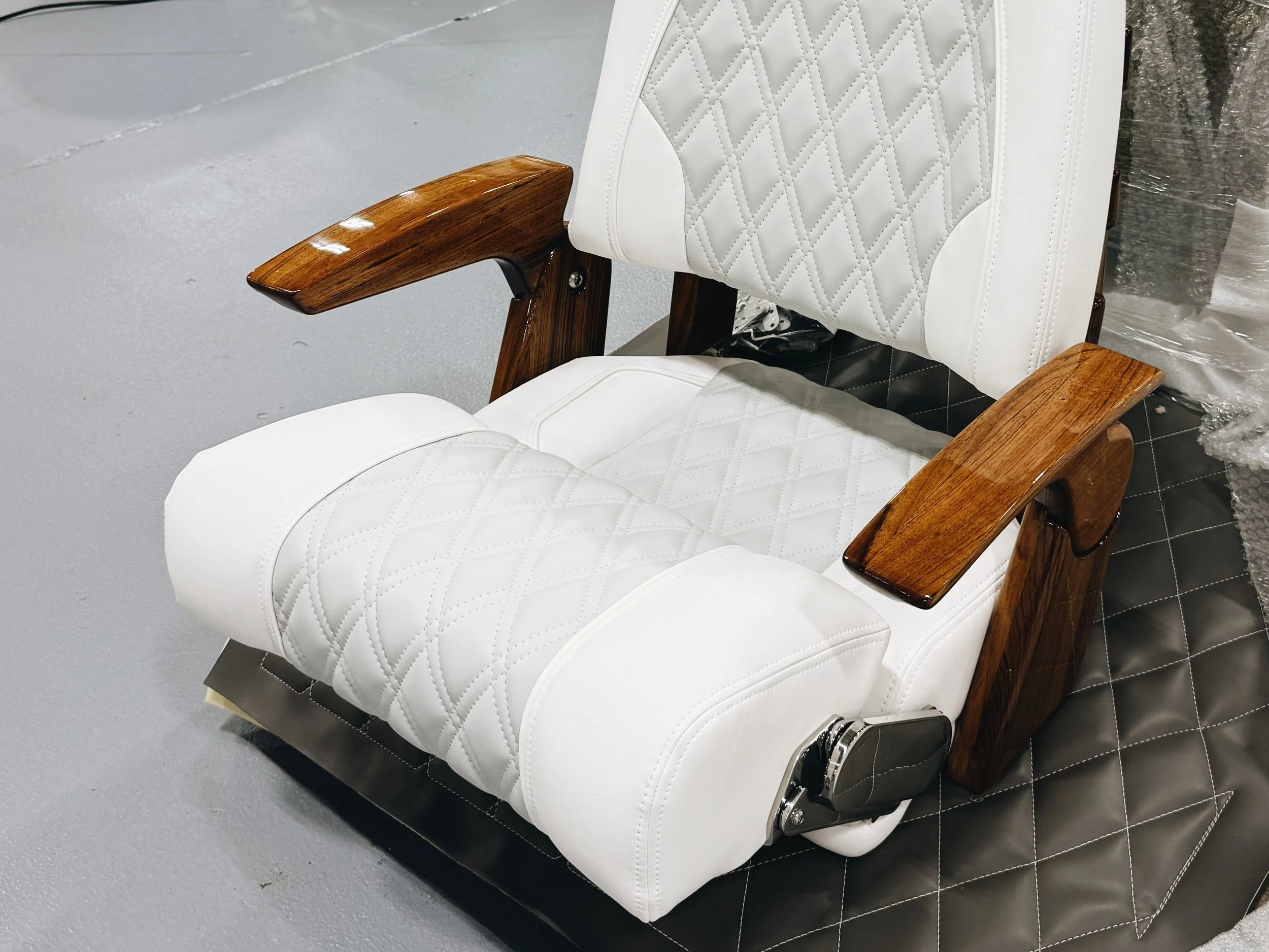 A white leather office chair with quilted pattern, wooden armrests, and adjustable mechanisms, placed on a padded black mat.