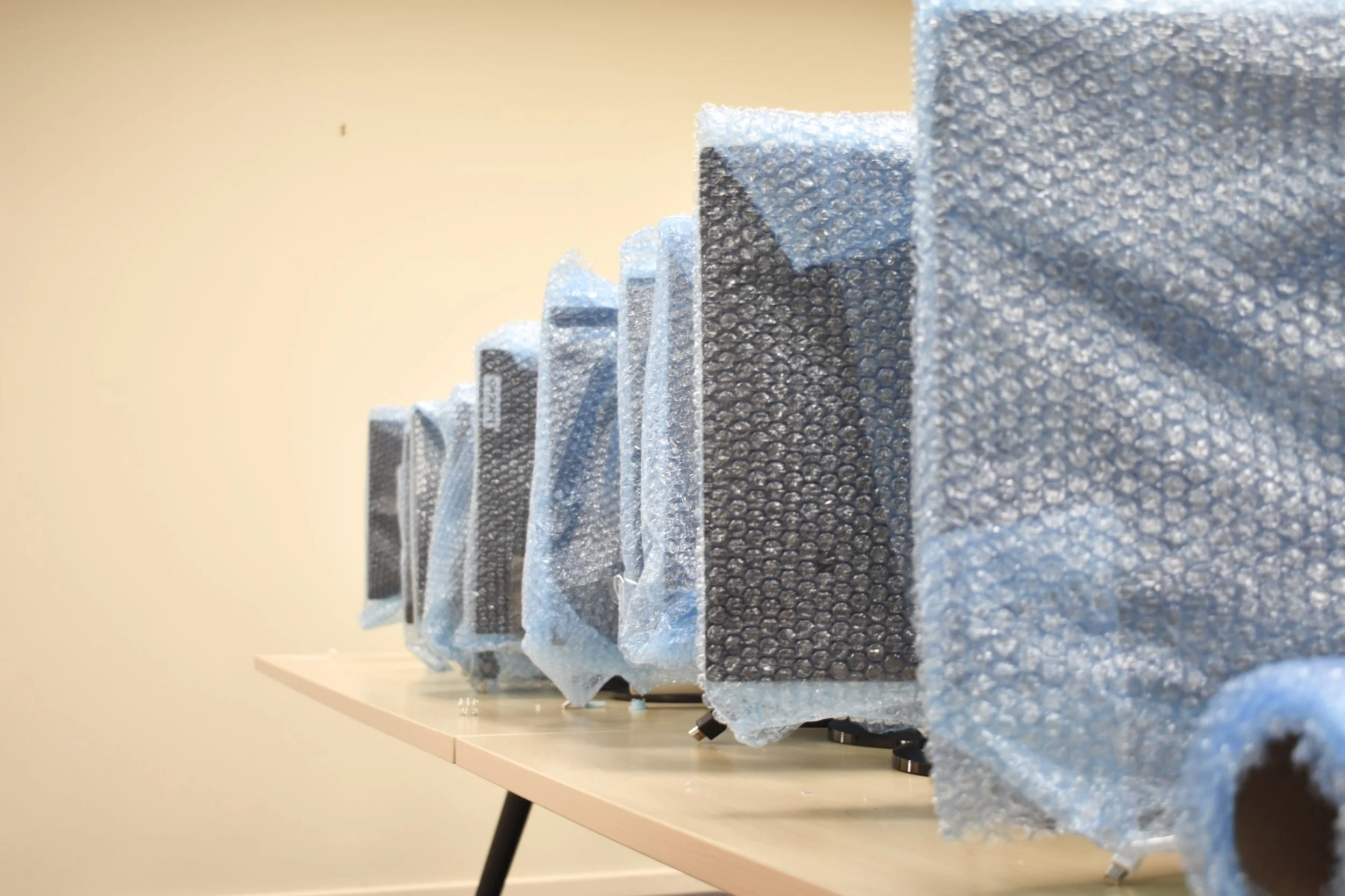 Four young men laughing and playing table tennis indoors in a room with beige walls and overhead fluorescent lights.