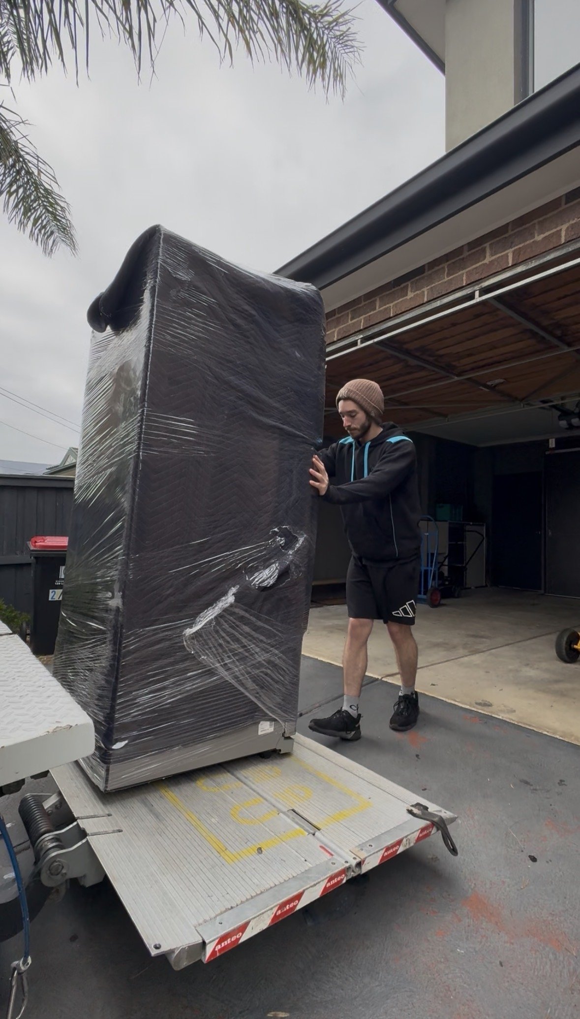 A man with tattoos on his arms assembling a wooden bed frame in a bedroom.
