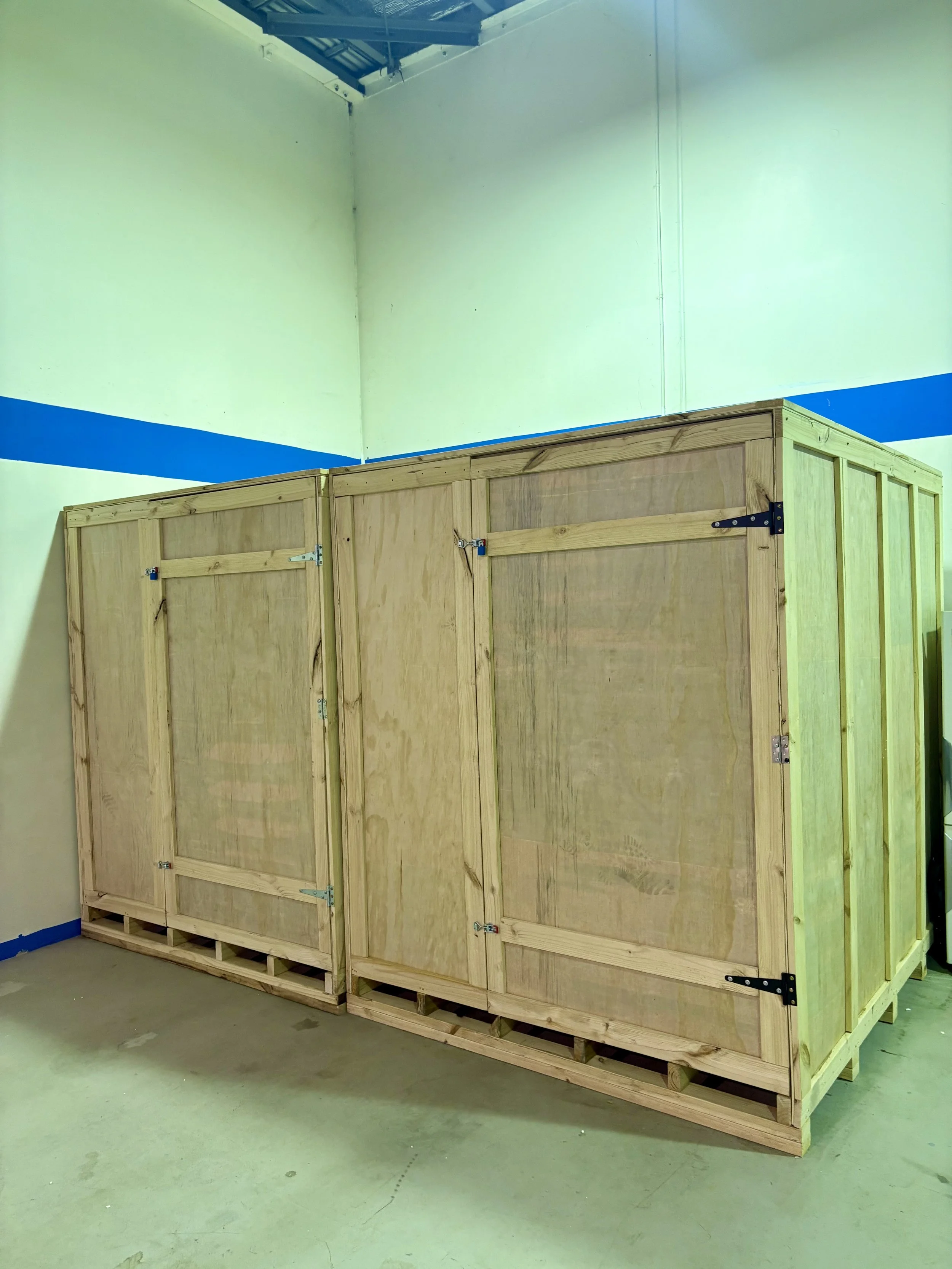 A person wrapping furniture with plastic wrap in a room filled with stacked furniture.