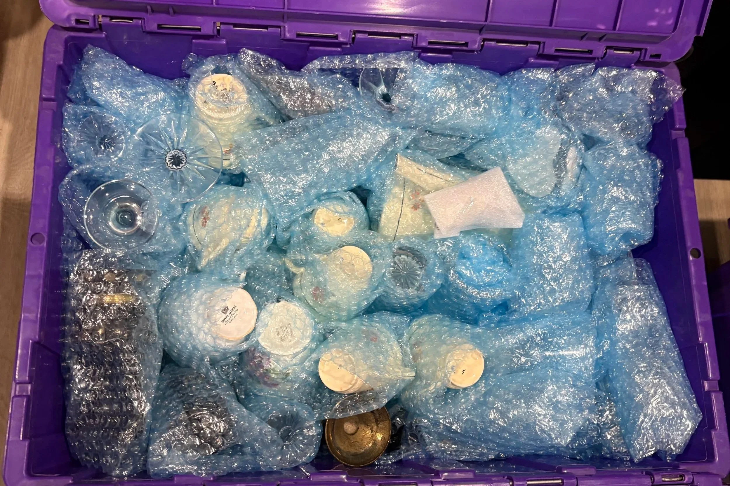 Stacks of purple plastic tubs labeled 'ecotub' at 'Cool Cat Removals' warehouse with a logo of a cat wearing sunglasses on the wall.