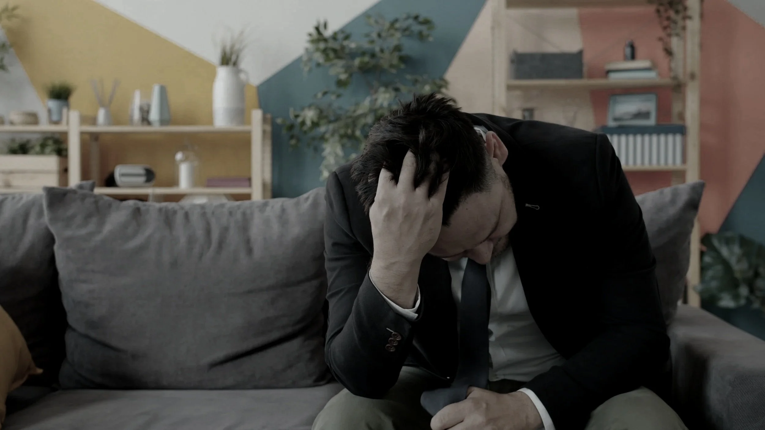 Man sitting on couch with head down looking worried