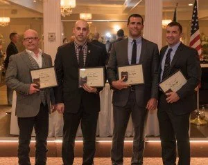 Four men in suits holding certificates at an award ceremony