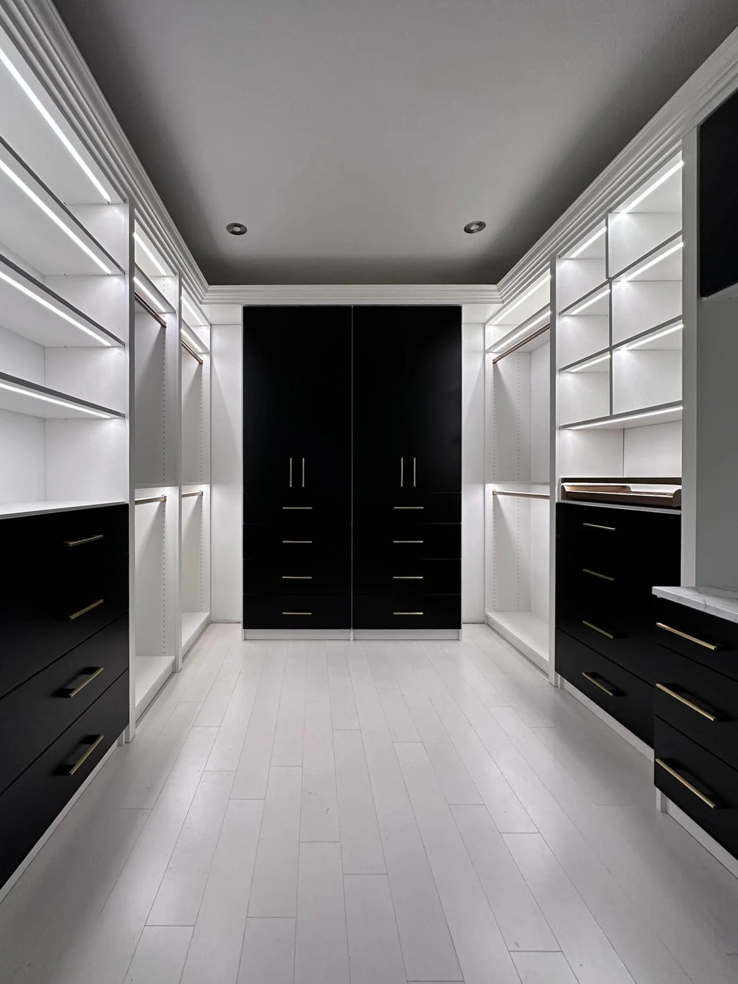 A modern walk-in closet with custom made black and white cabinetry and open shelves and accent lighting.