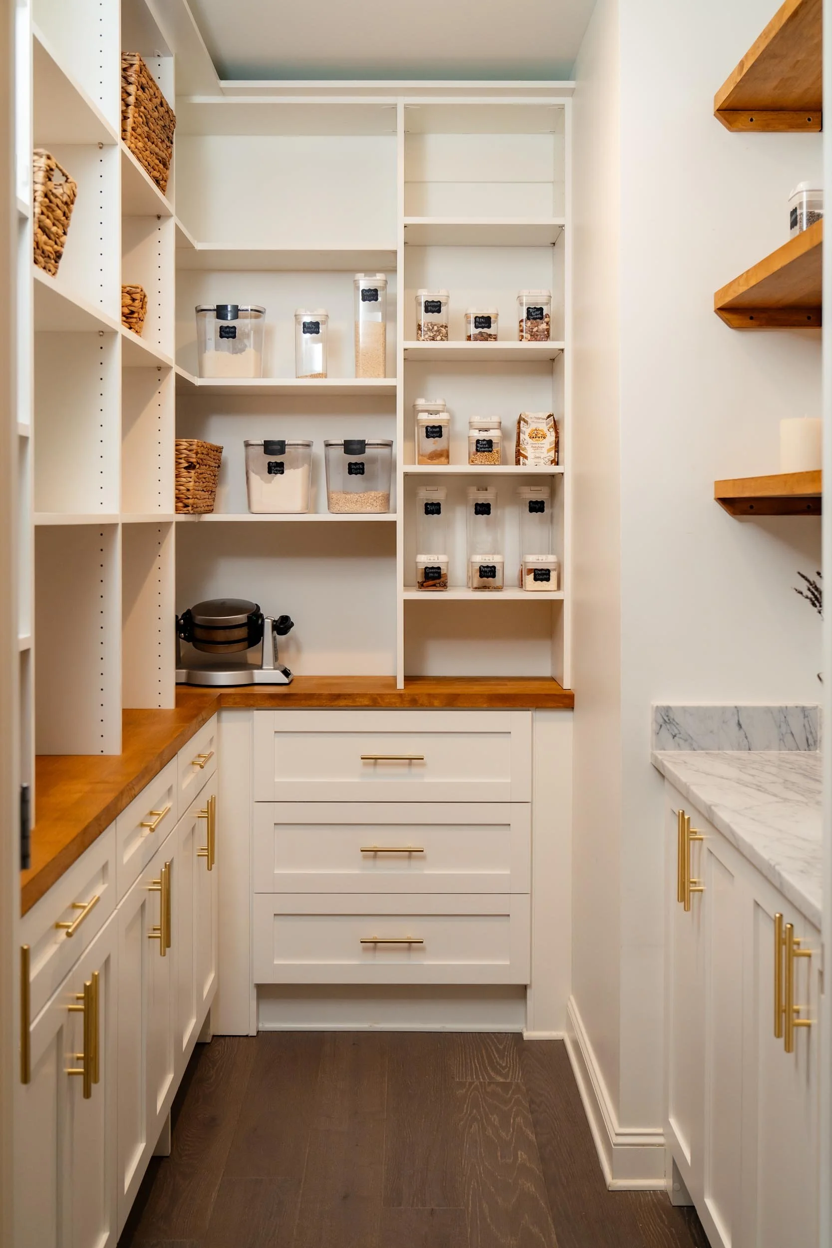 Walk-in pantry with white custom shelving and storage, wooden countertops, and accent lighting.