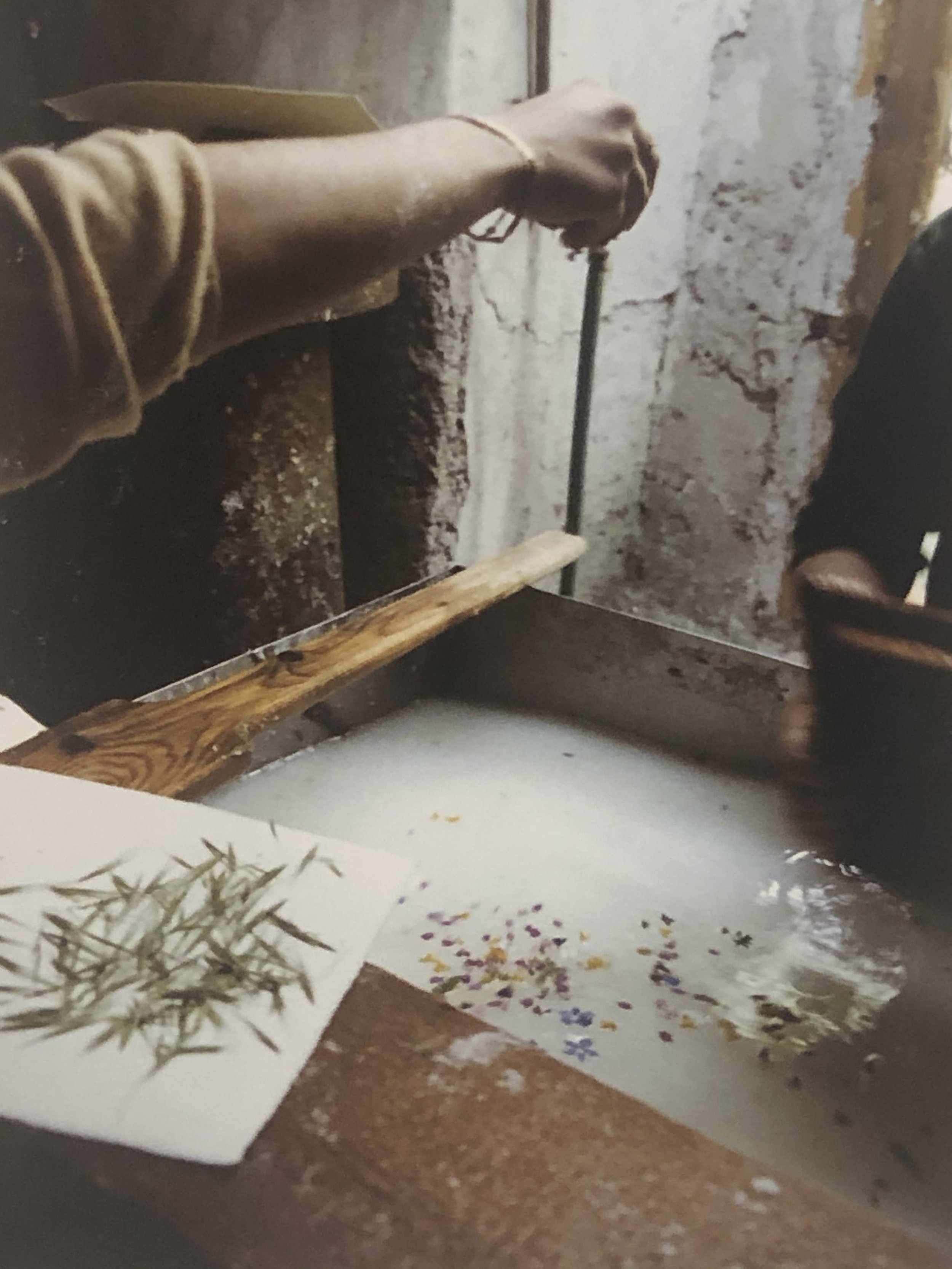 Artist at the Amatruda paper mill adding flower petals to handmade cotton paper during the papermaking process.