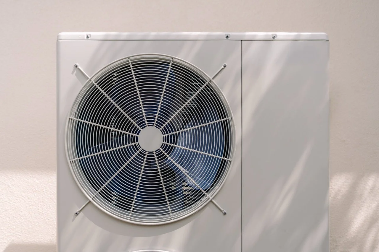 White air conditioning unit with large circular fan protected by a metal grille, mounted on a wall.
