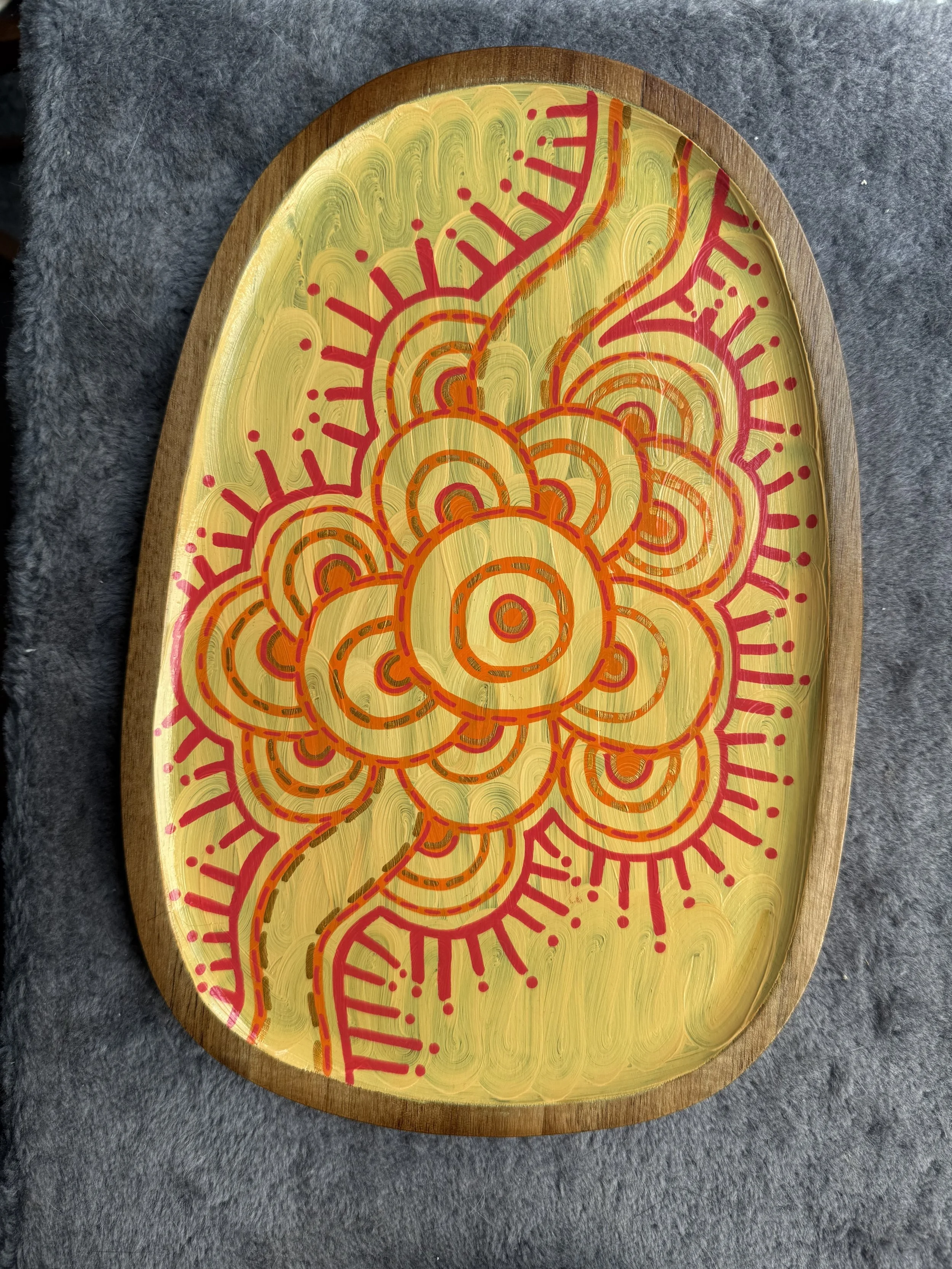 Decorative tray with a yellow background and red abstract floral patterns on a gray fabric surface.