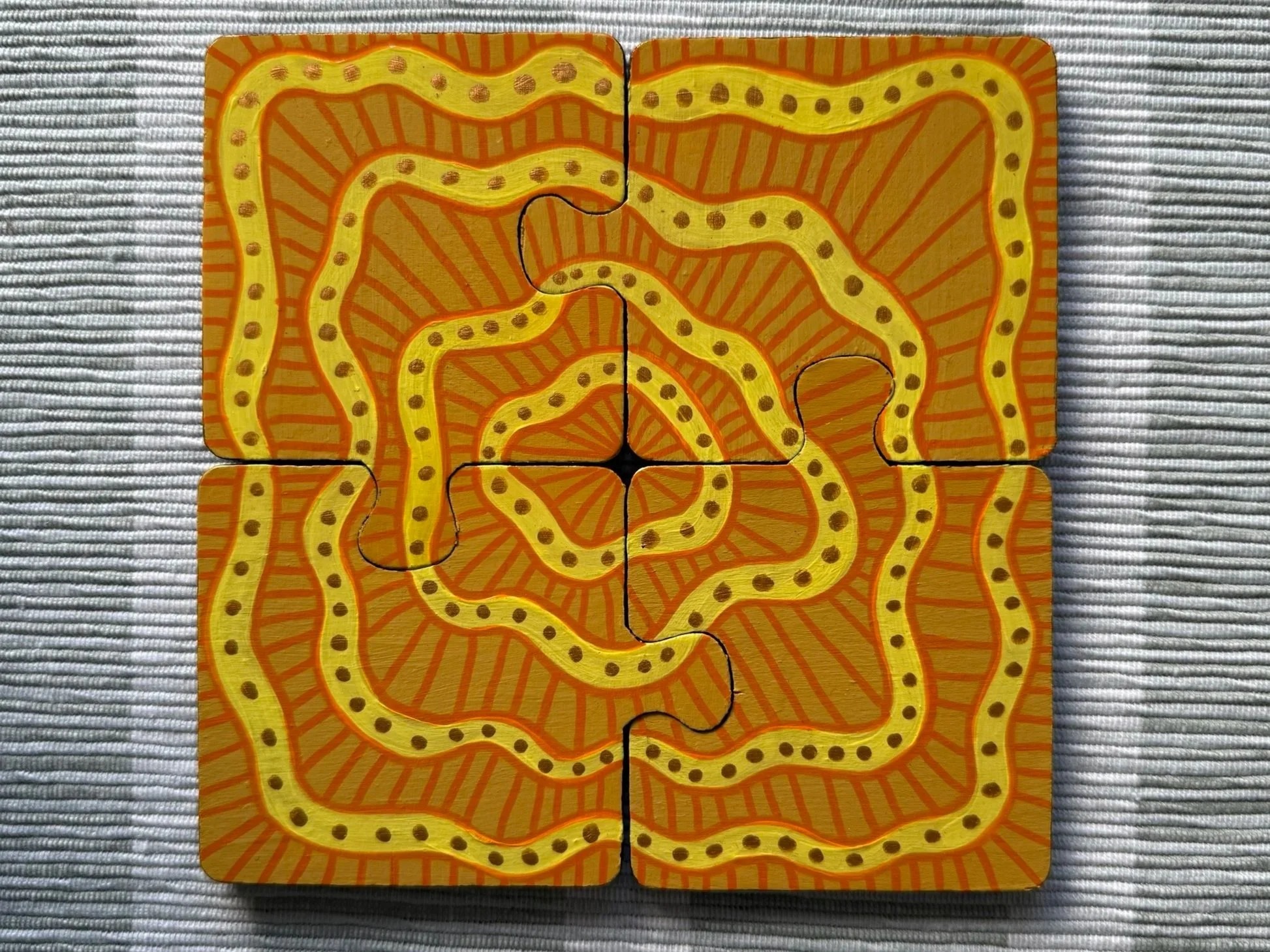 Four interconnected puzzle pieces with a yellow and orange abstract spiral pattern, placed on a textured gray surface.