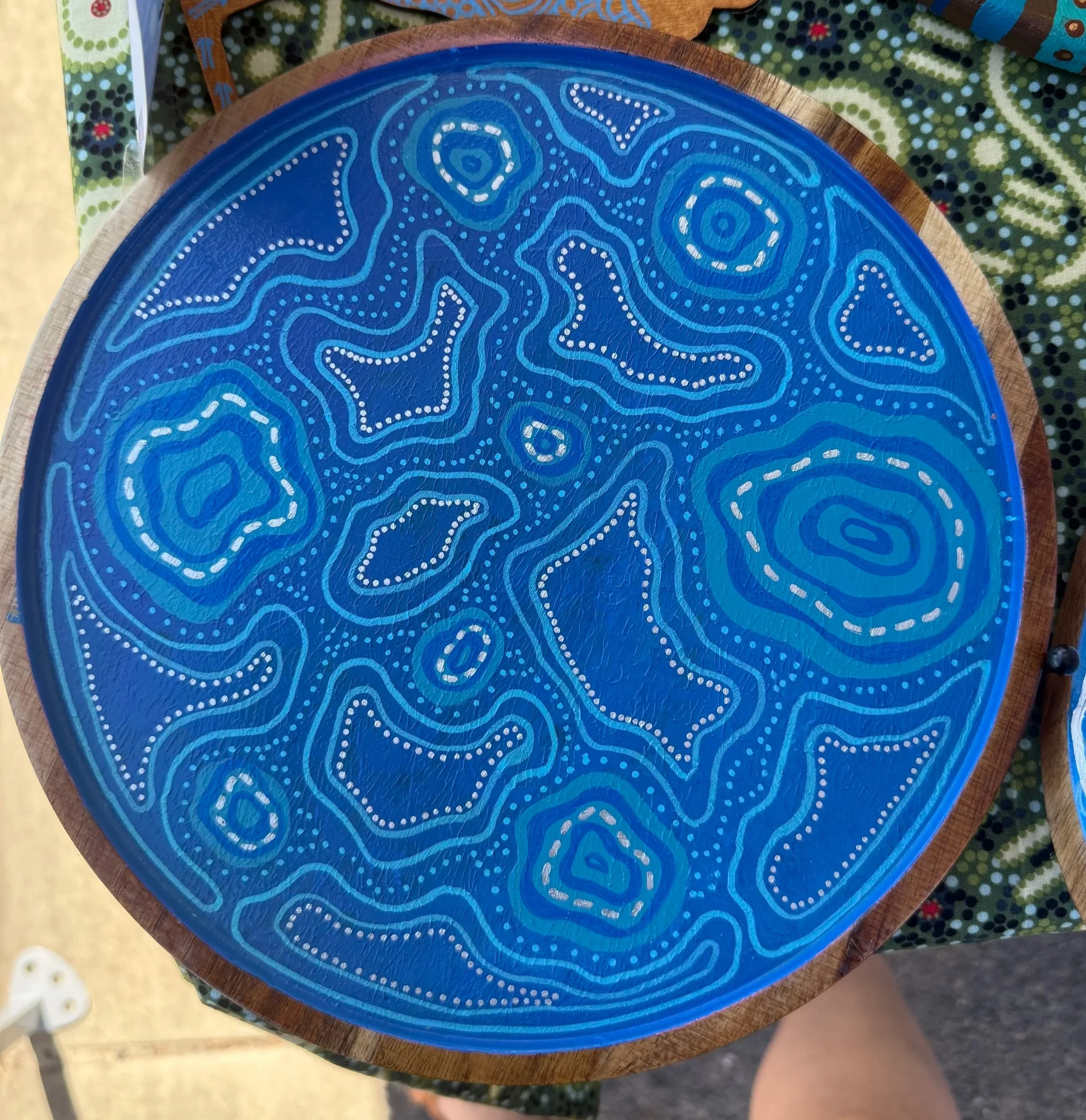 Circular wooden tray with a blue painted surface featuring white dot patterns and abstract shapes.