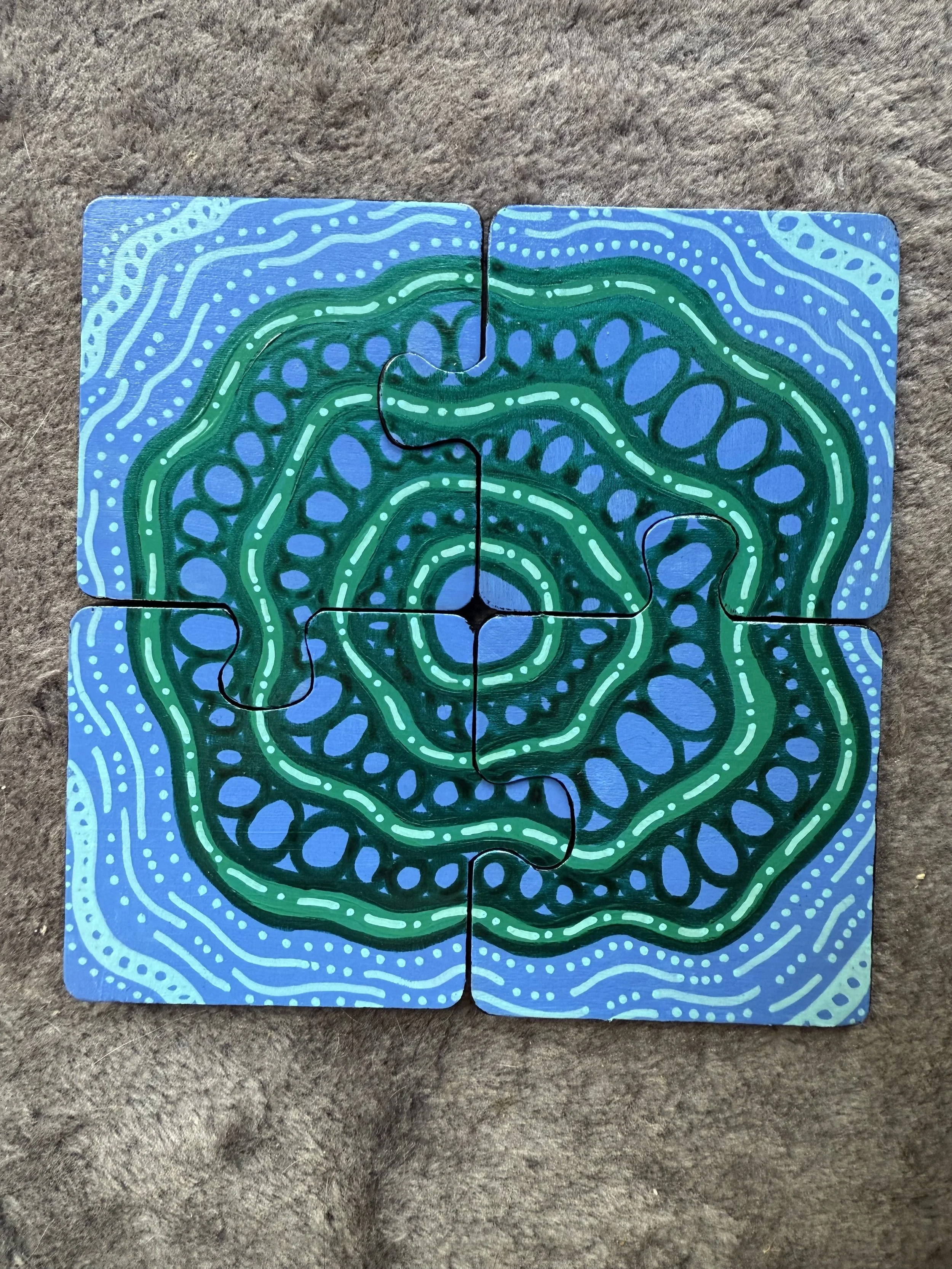 Four puzzle pieces forming a square with a colorful, abstract mandala-like design in shades of blue and green on a textured surface.