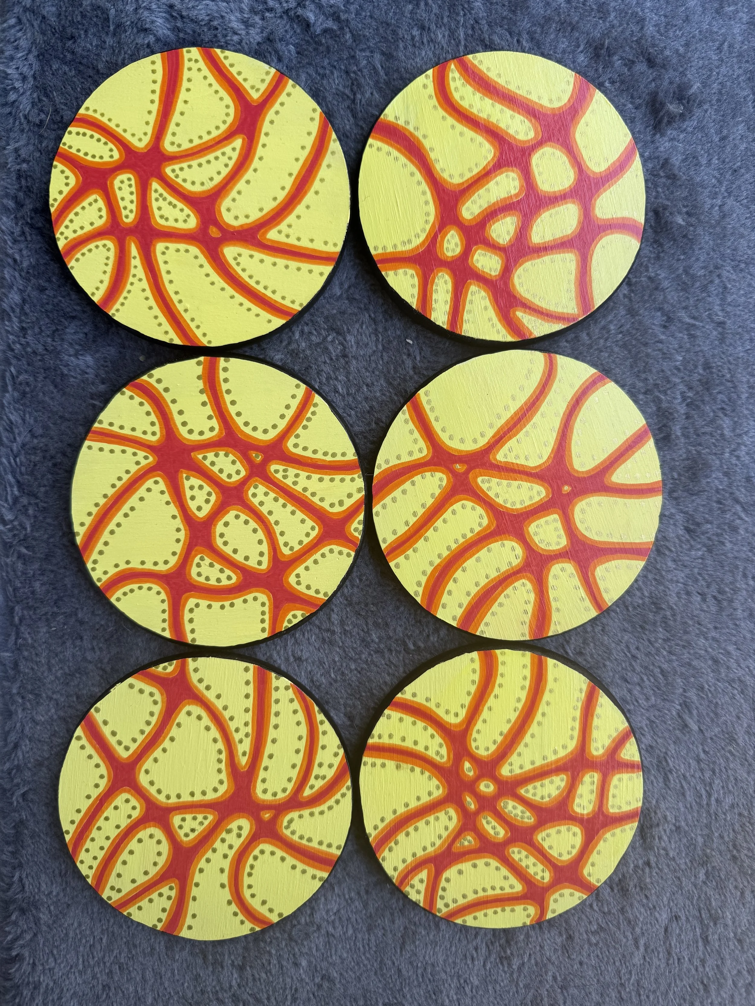 Six circular coasters with a yellow background and red-orange web-like pattern, placed on a dark gray surface.