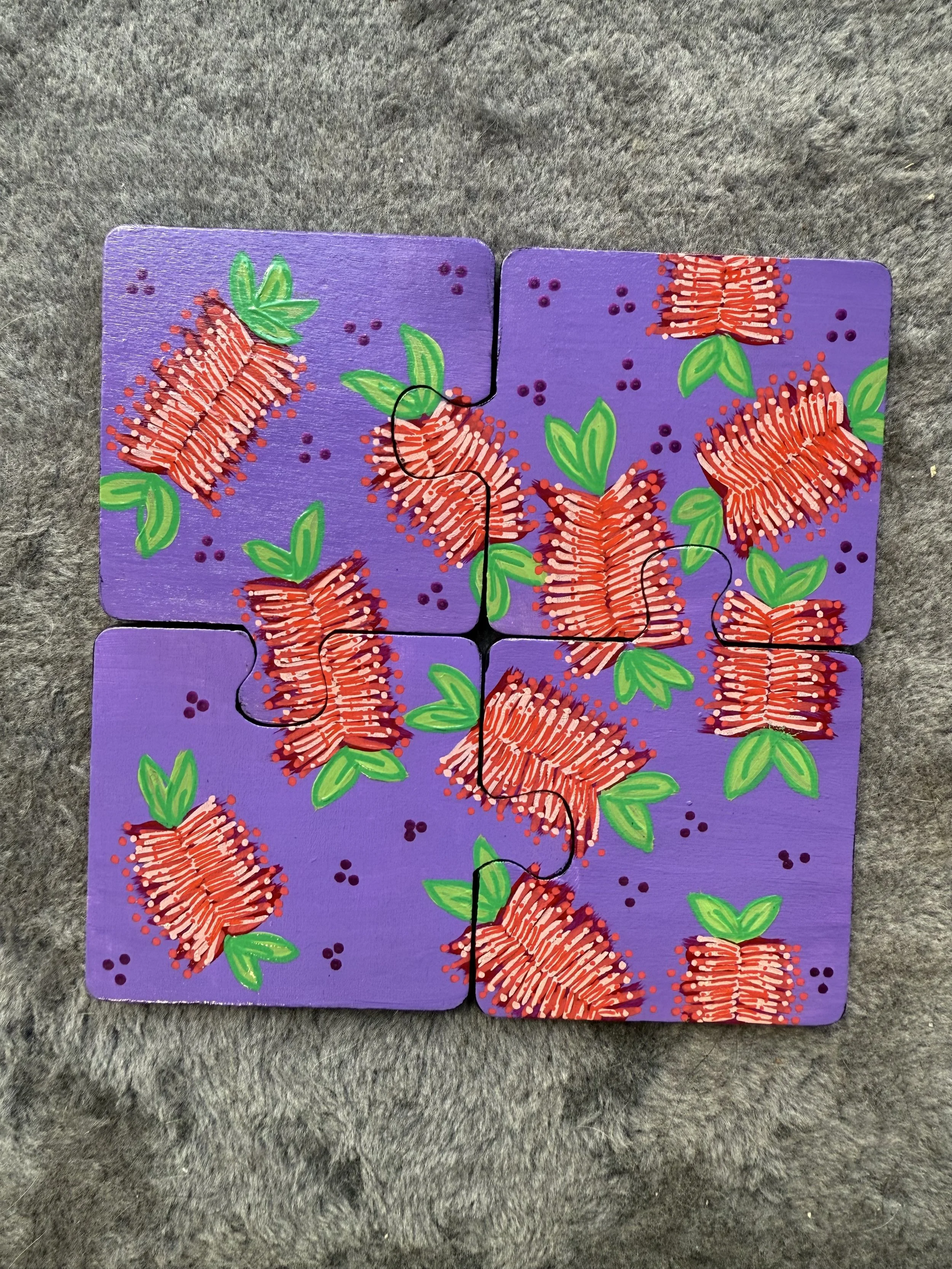 Colorful puzzle with a purple background, featuring red flowers with green leaves and small purple dots, assembled on a gray textured surface.