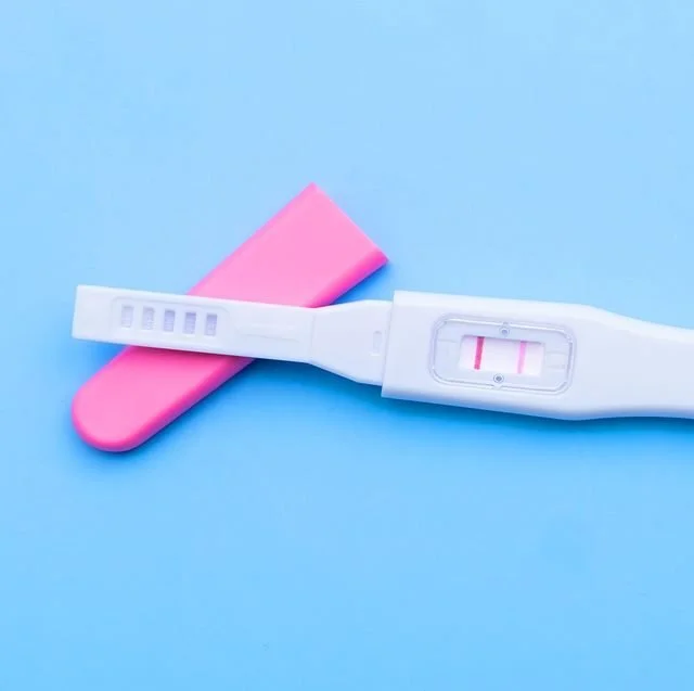 Positive pregnancy test on a pink and blue background.