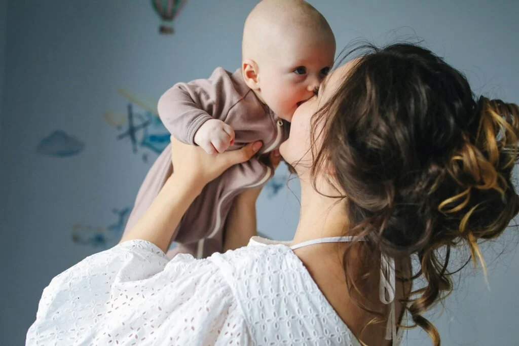 A woman holding a baby up and kissing the baby on the lips.