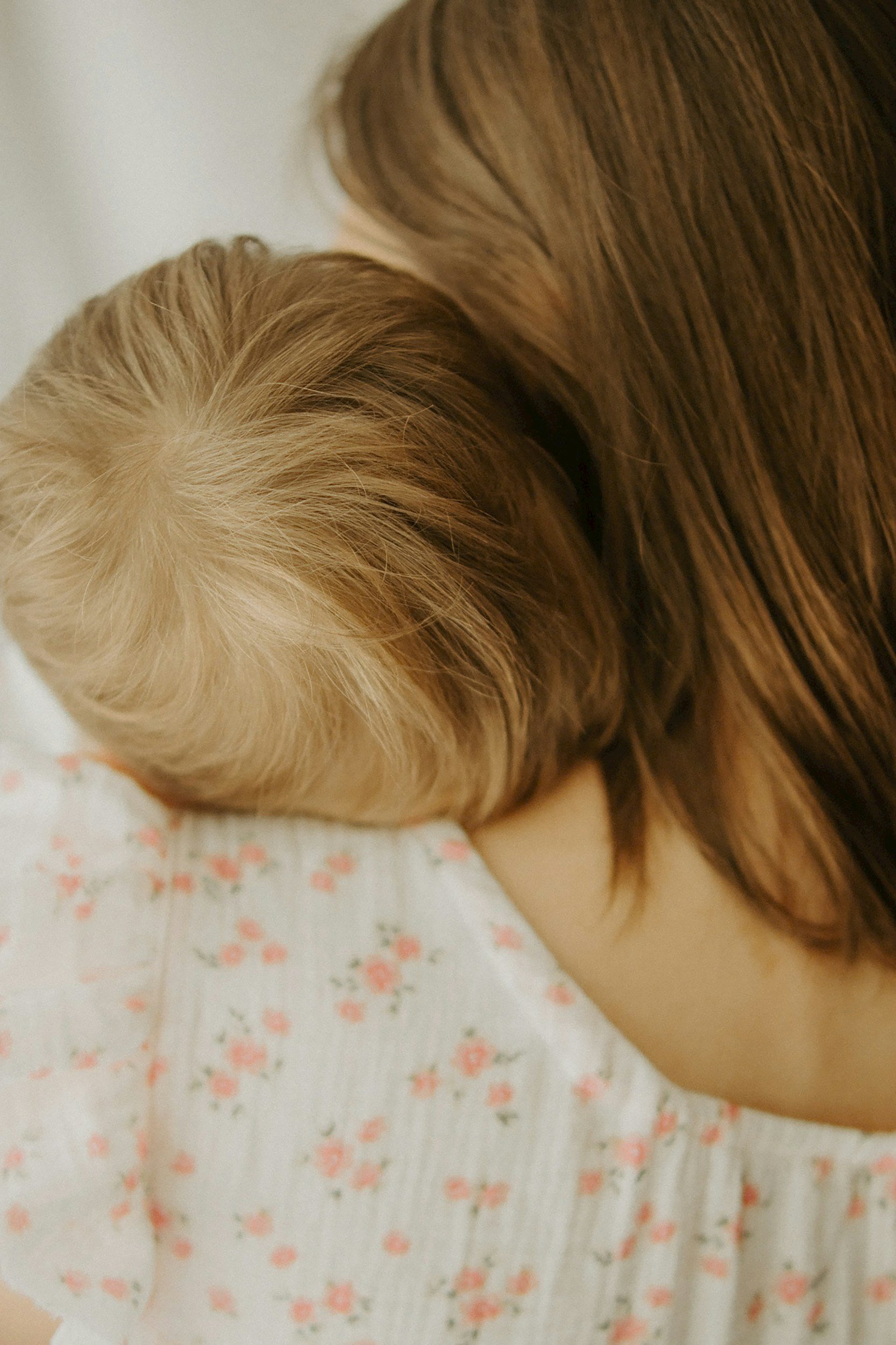 A person with brown hair is holding a child with blonde hair close in a comforting embrace.