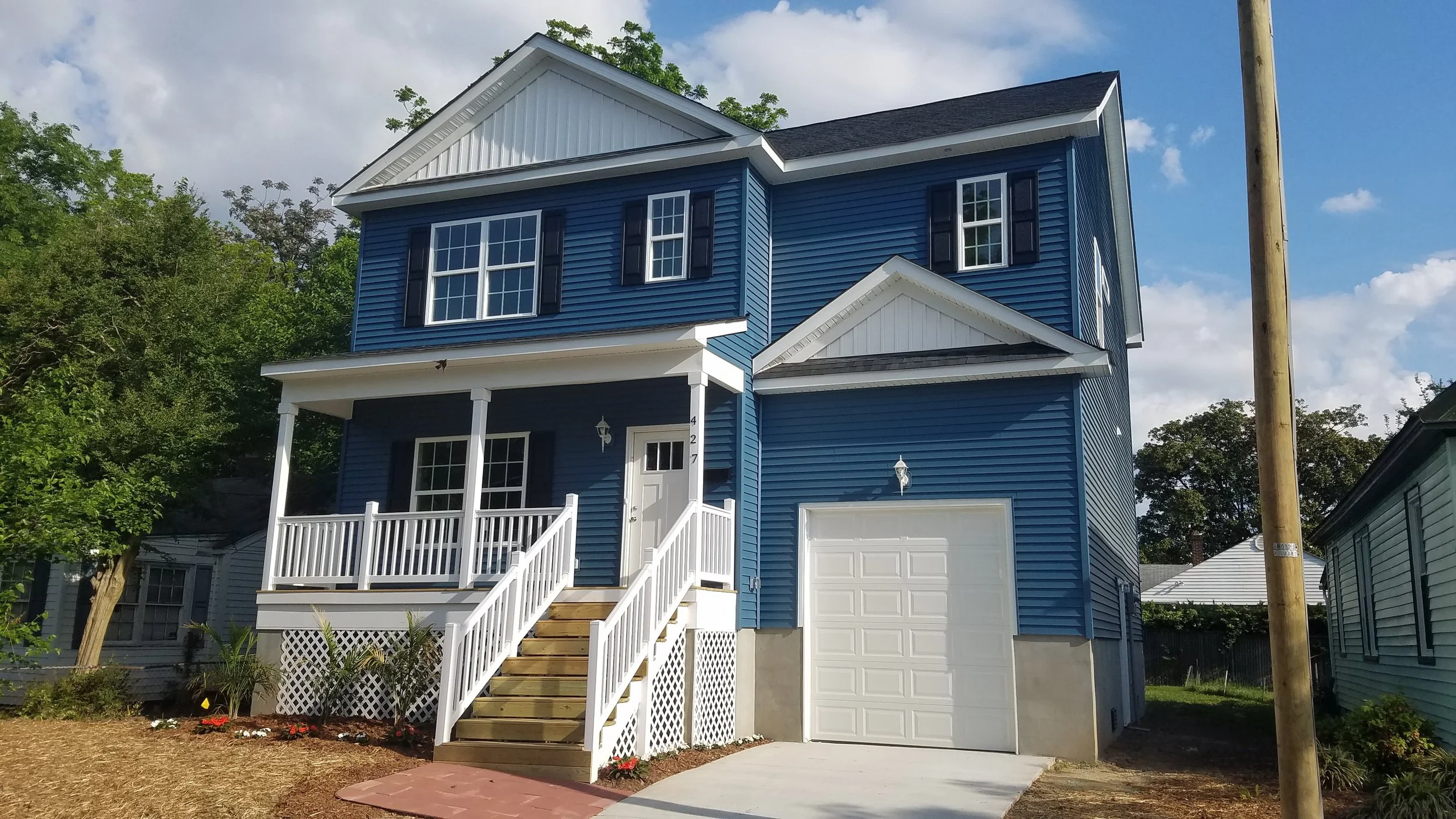 A completed two-story single-family house with white trim, black window shutters, a small front porch with stairs and an attached garage.