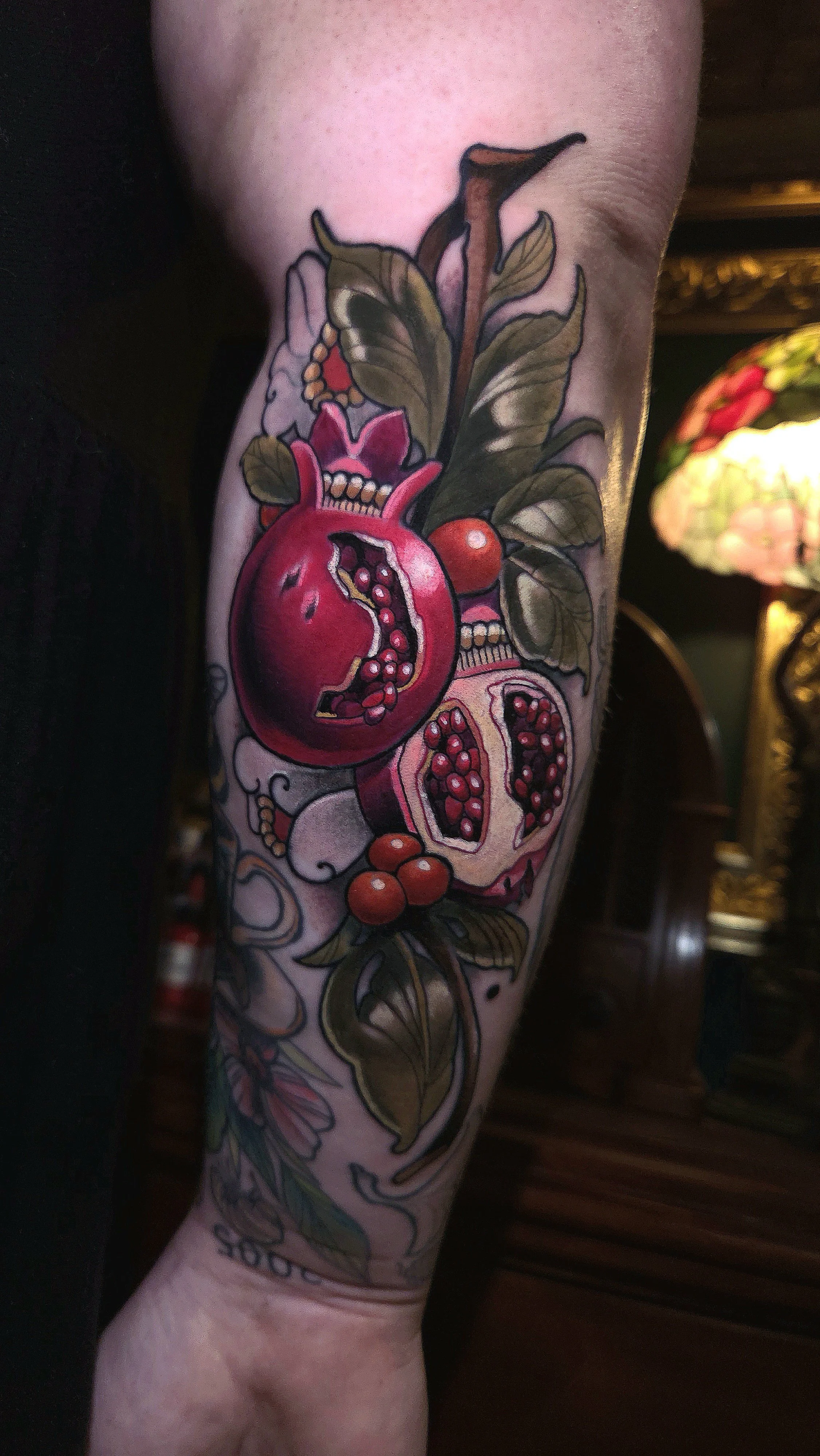 Colorful tattoo of pomegranate fruit and leaves on an arm.