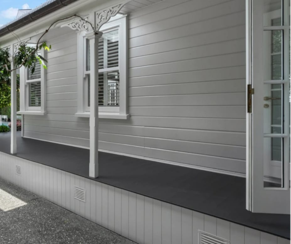Exterior view of a white house with siding, two windows with shutters, a door with a glass panel, and a porch with a dark floor and decorative white supports.
