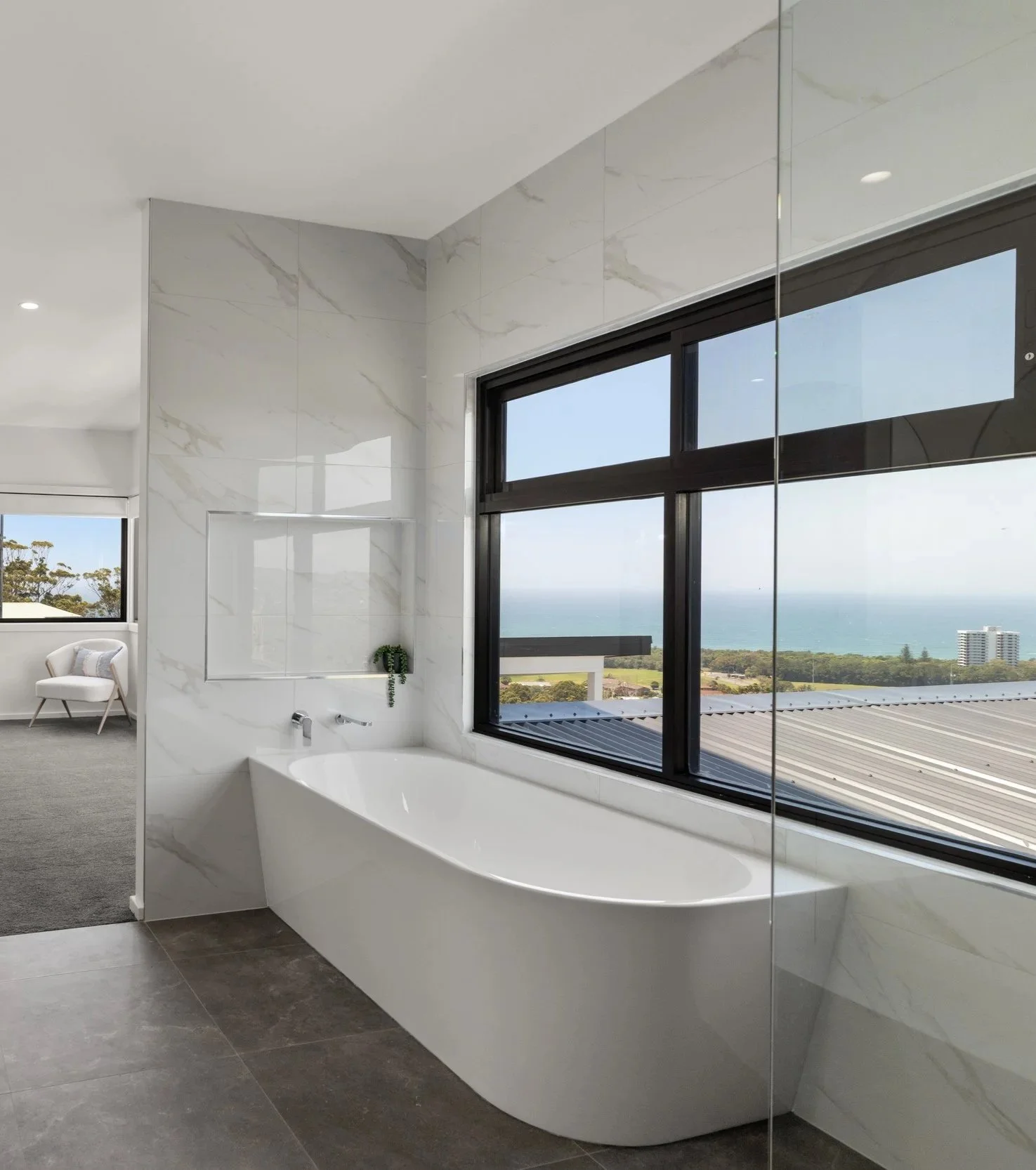 Modern bathroom with a white bathtub near large windows overlooking a scenic ocean view.