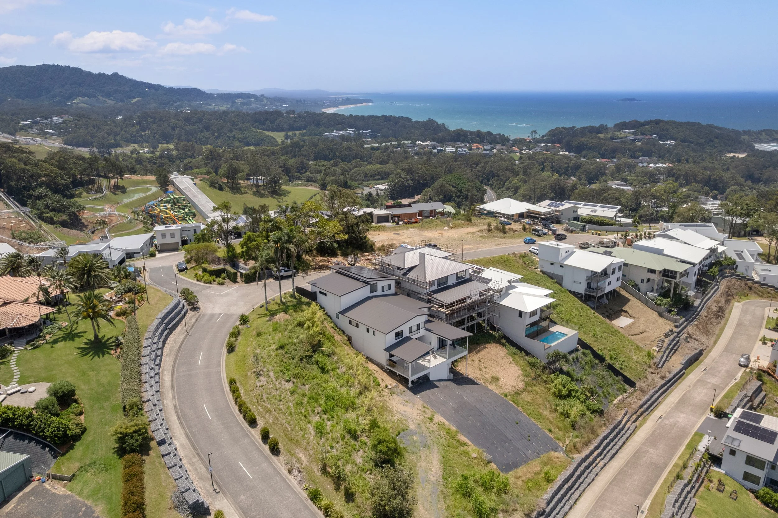 Aerial view of a residential neighborhood near the coastline with houses, a winding road, and a park with a playground.