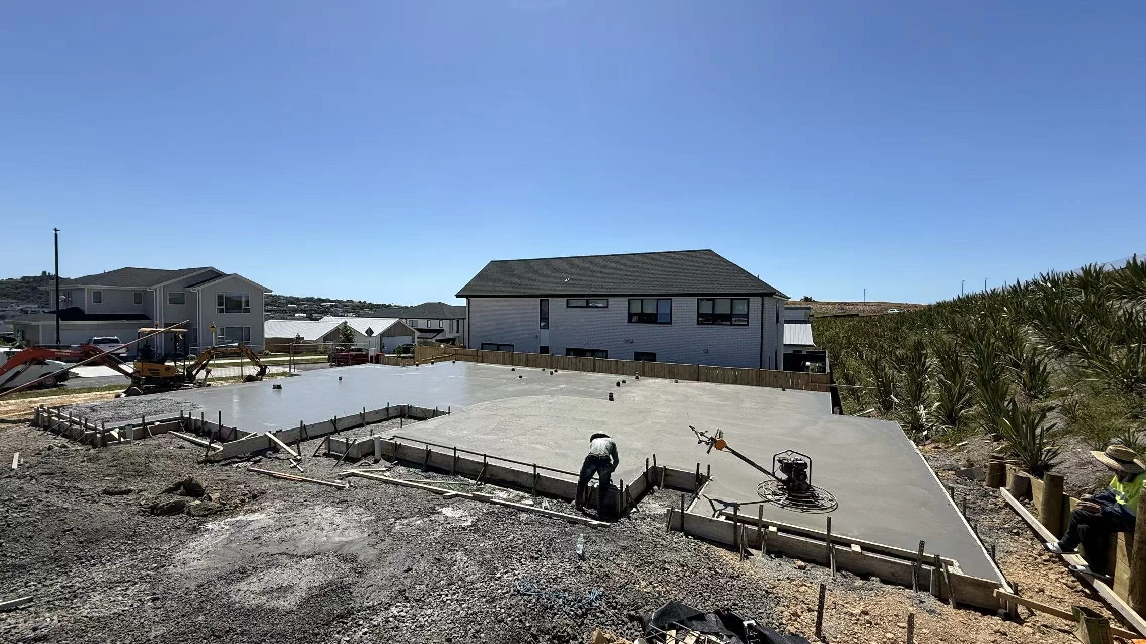 Professional concrete laying for a RibRaft foundation integrated with a structural block wall perimeter, showcasing precision finishing on a high-spec residential build in Auckland.