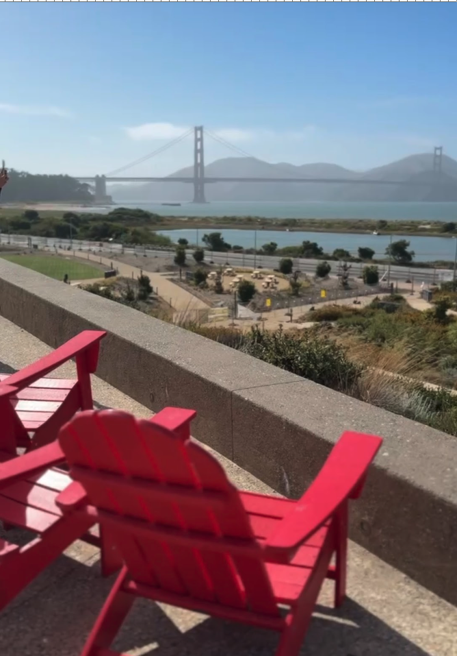 Two red wooden chairs on a balcony overlooking a coastal landscape with a bridge in the background.