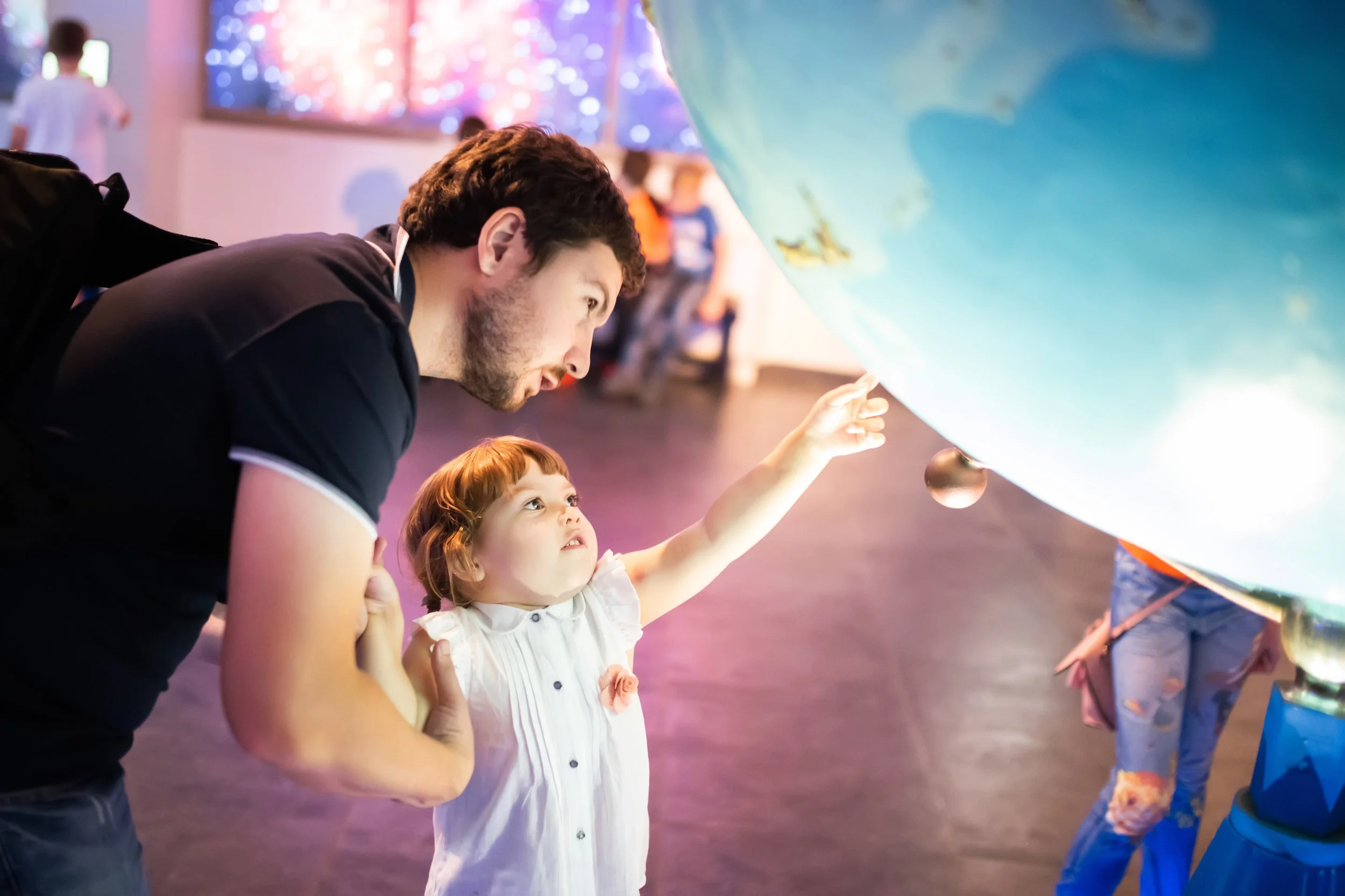 A man and a young girl are looking and pointing at a large globe display in what appears to be a museum or science center.
