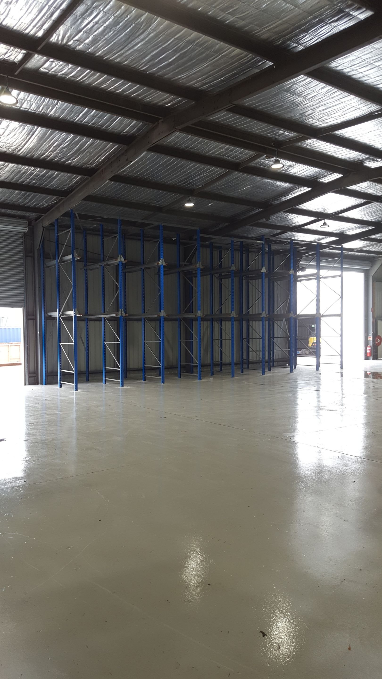 Inside an empty warehouse with metal shelving units, polished concrete floor, and high ceiling with insulation panels.