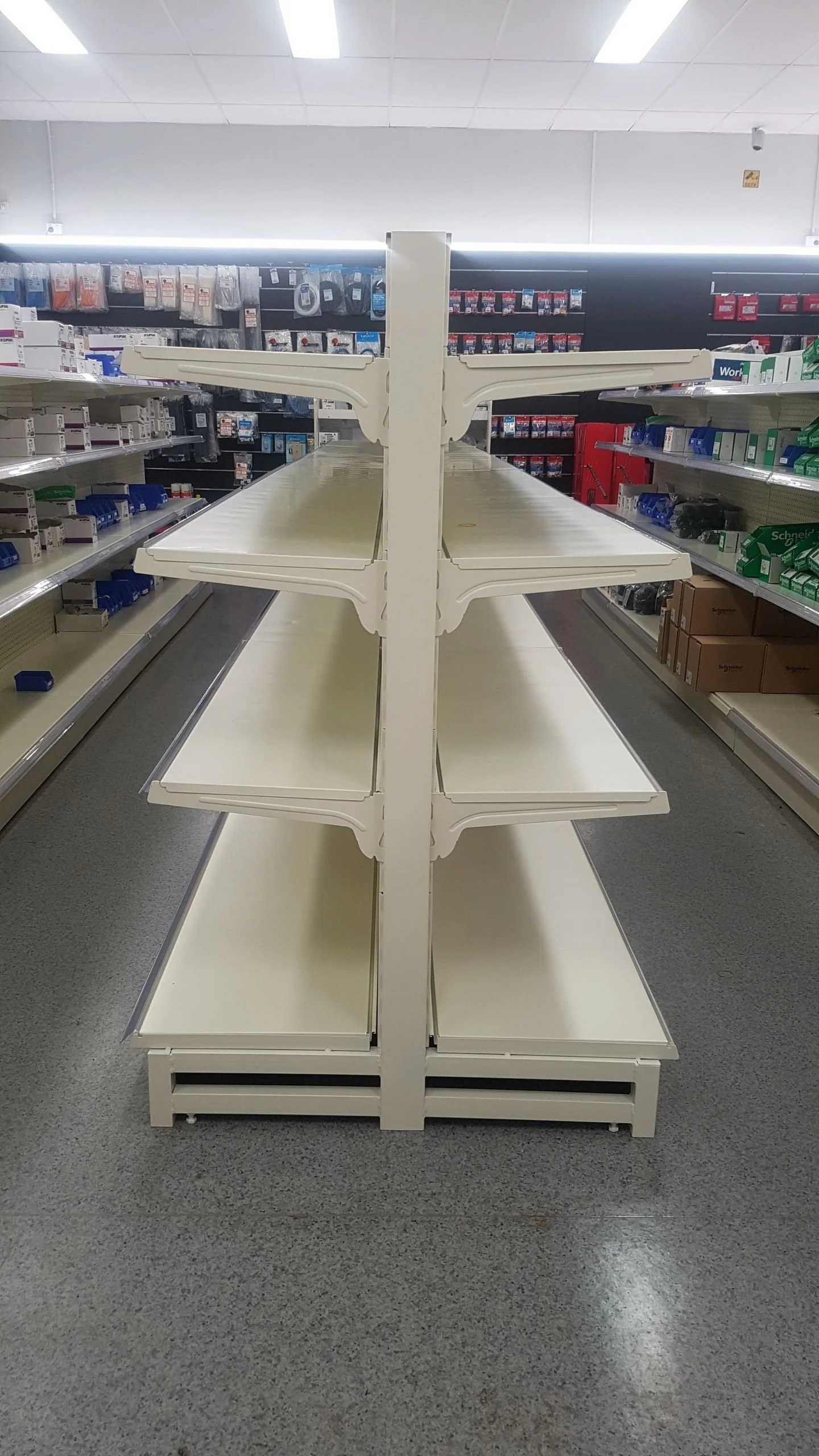 Empty white store shelves with multiple tiers in a retail store aisle.