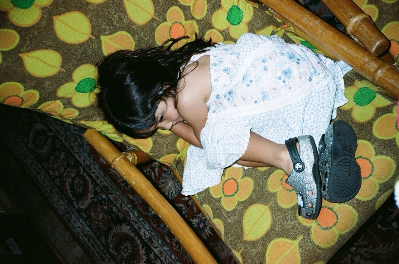 A young girl with dark hair sleeping on a floral patterned bed with her head resting on her arm.